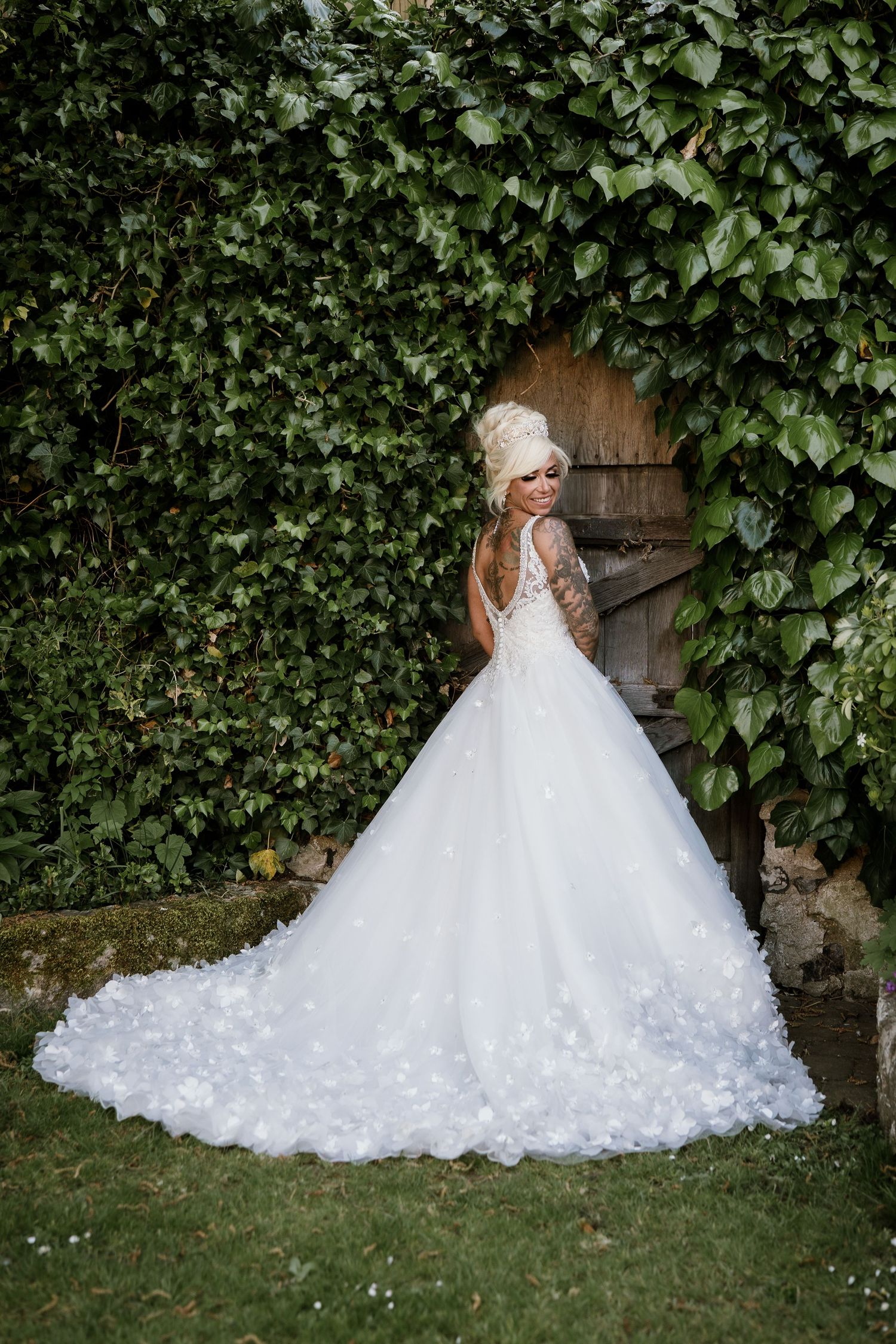 A stunning lace wedding dress with long train photographed against an ivy-covered wall.