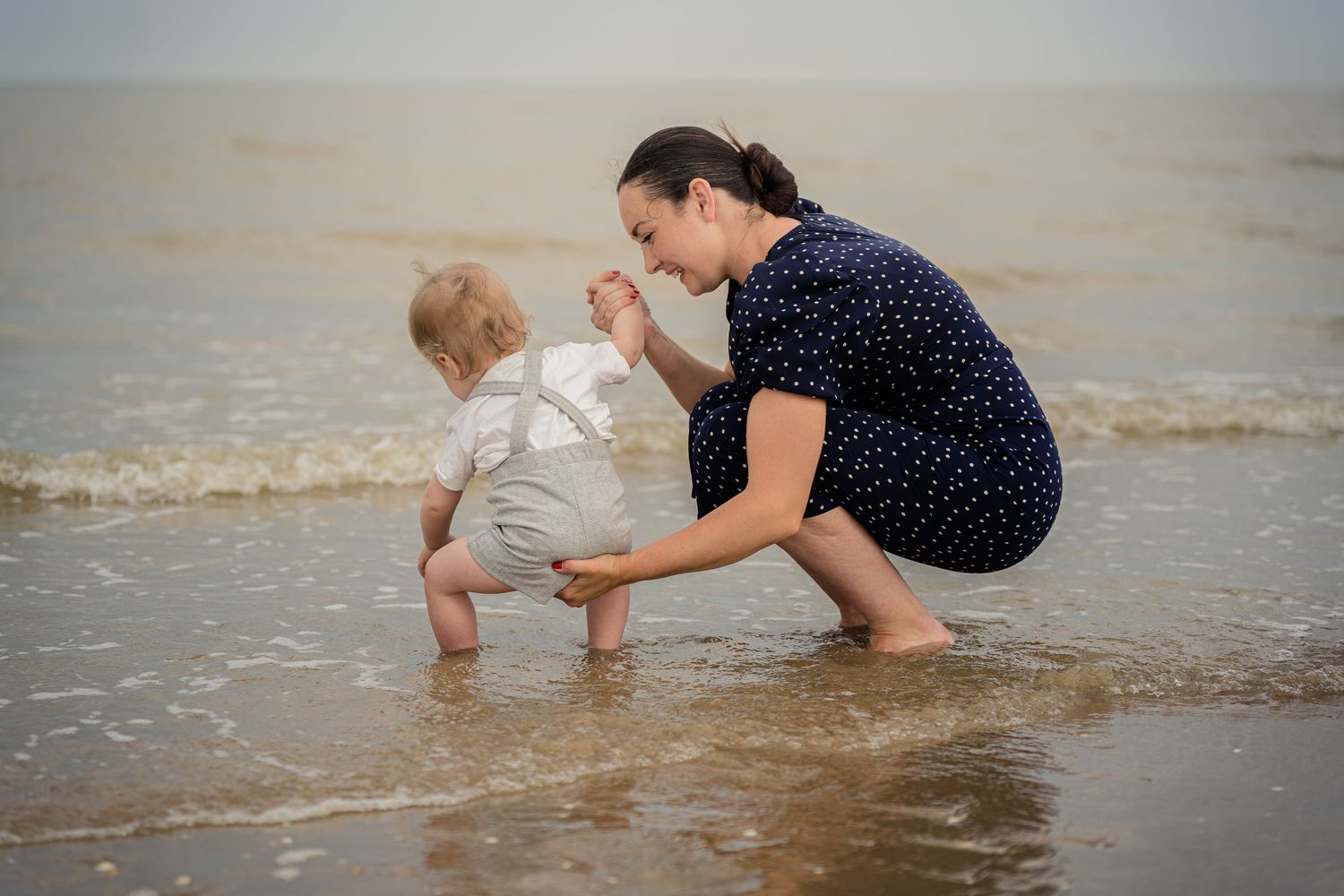 Two people playing together at the edge of the ocean waves on a sandy beach.
