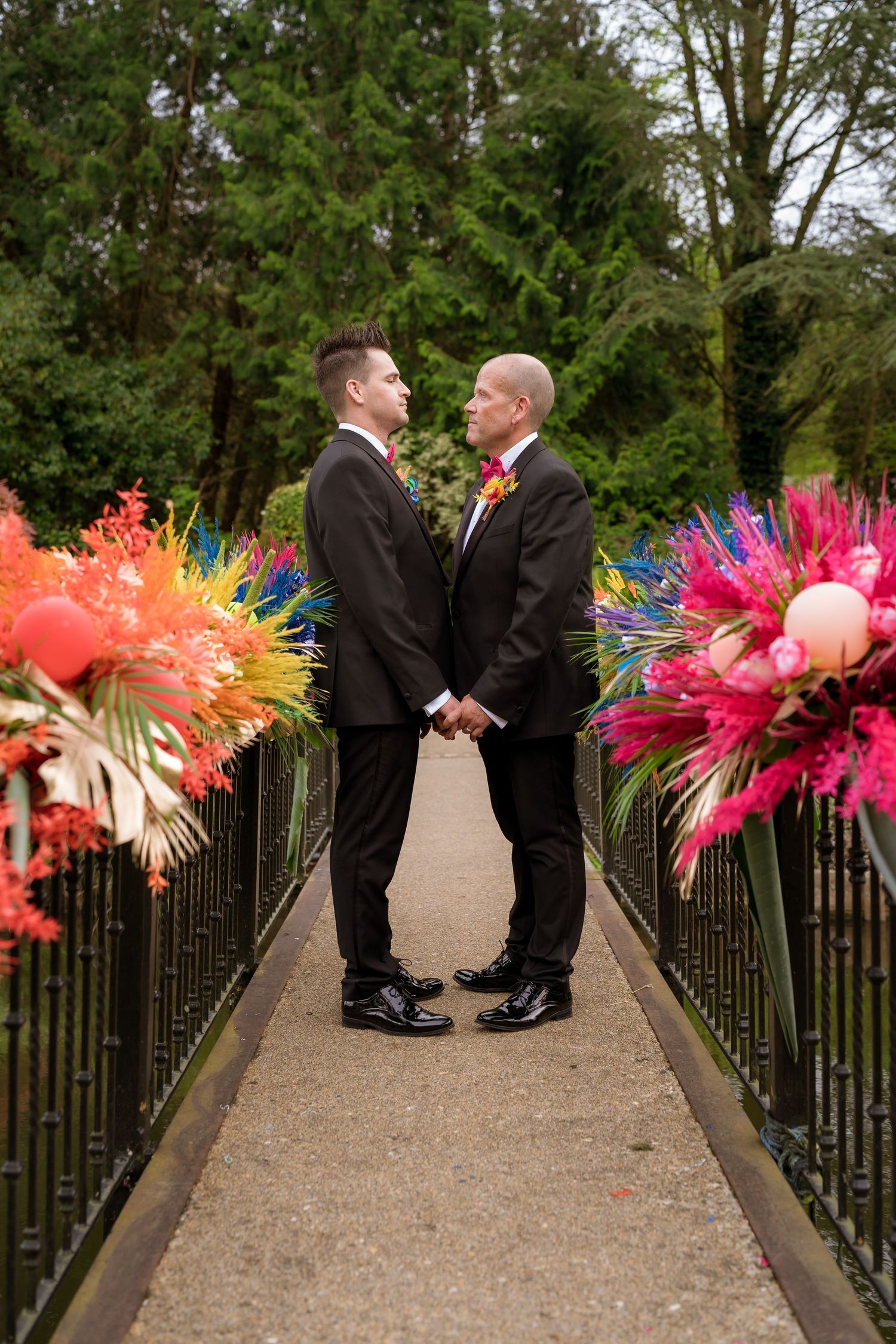 Wedding couple stands on a bridge decorated with vibrant colorful floral arrangements and balloons.