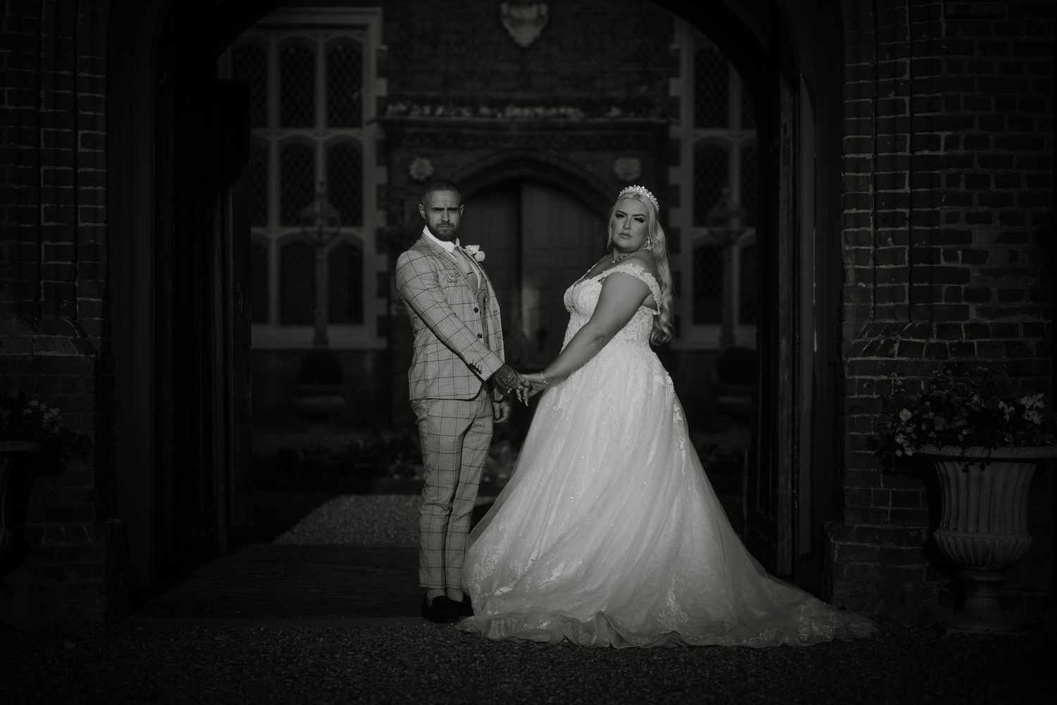 A black and white wedding portrait under a vintage brick archway entrance.