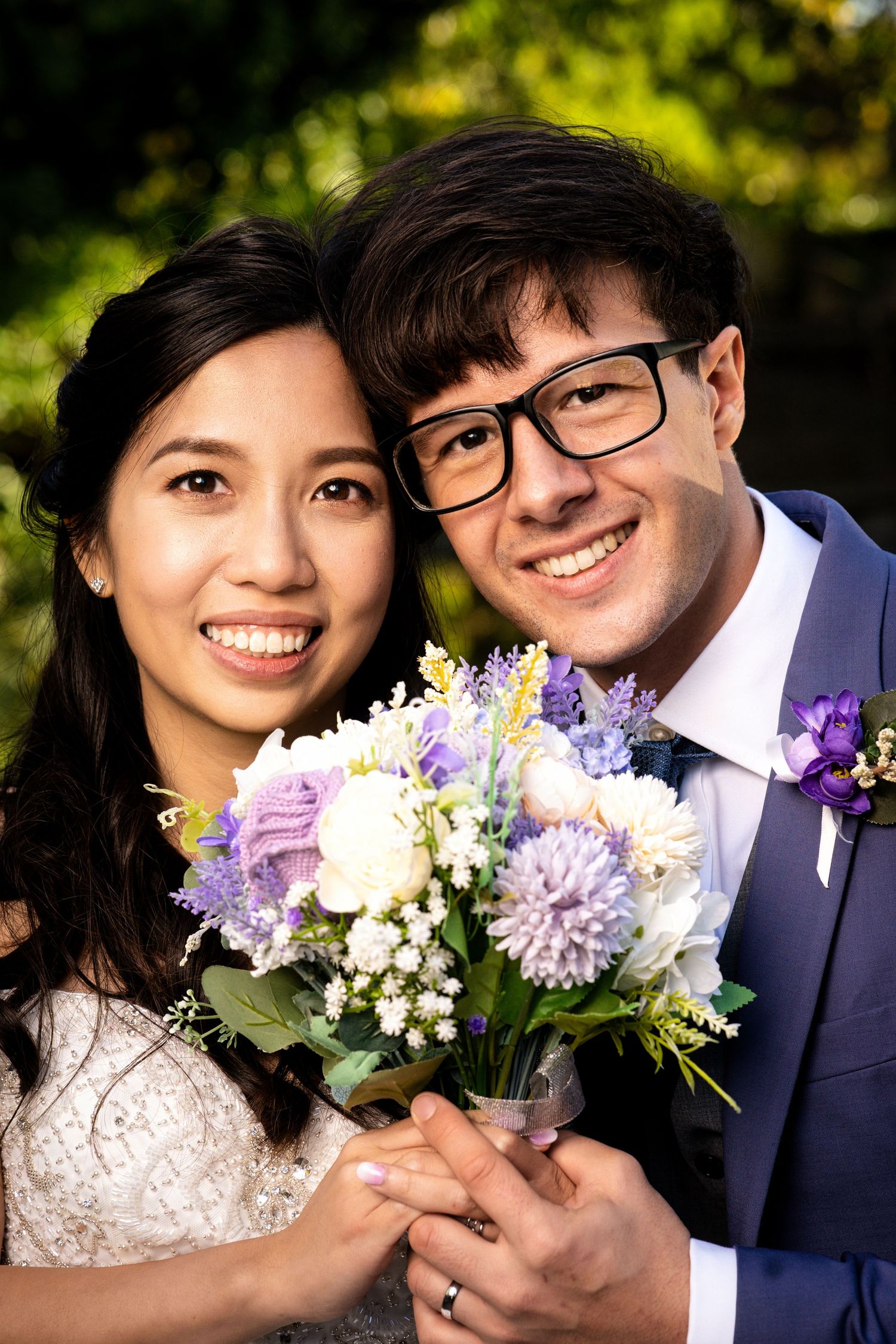 A couple poses with a beautiful purple and white wedding bouquet.