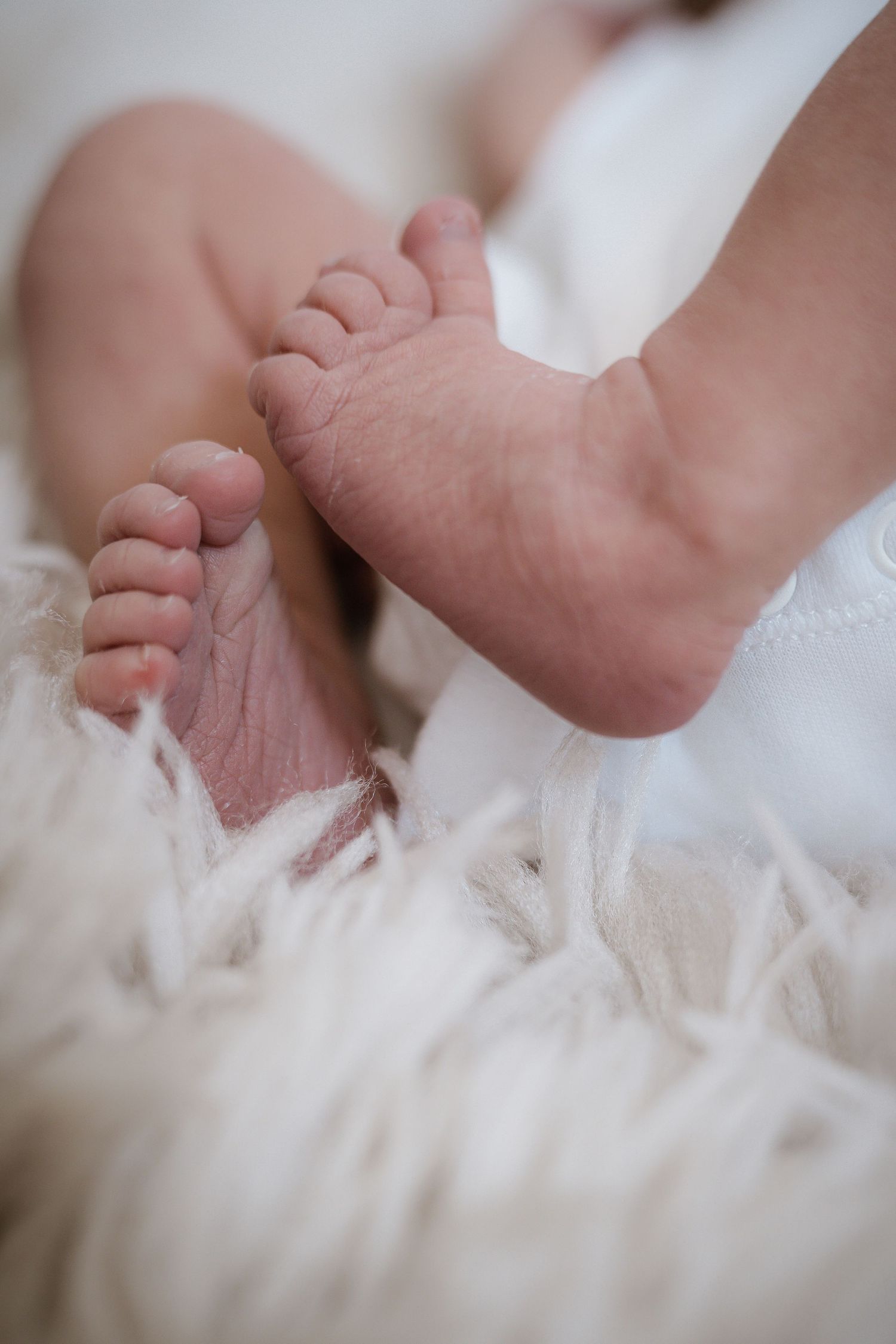 Tiny newborn baby feet resting on soft white fur blanket in close-up view.