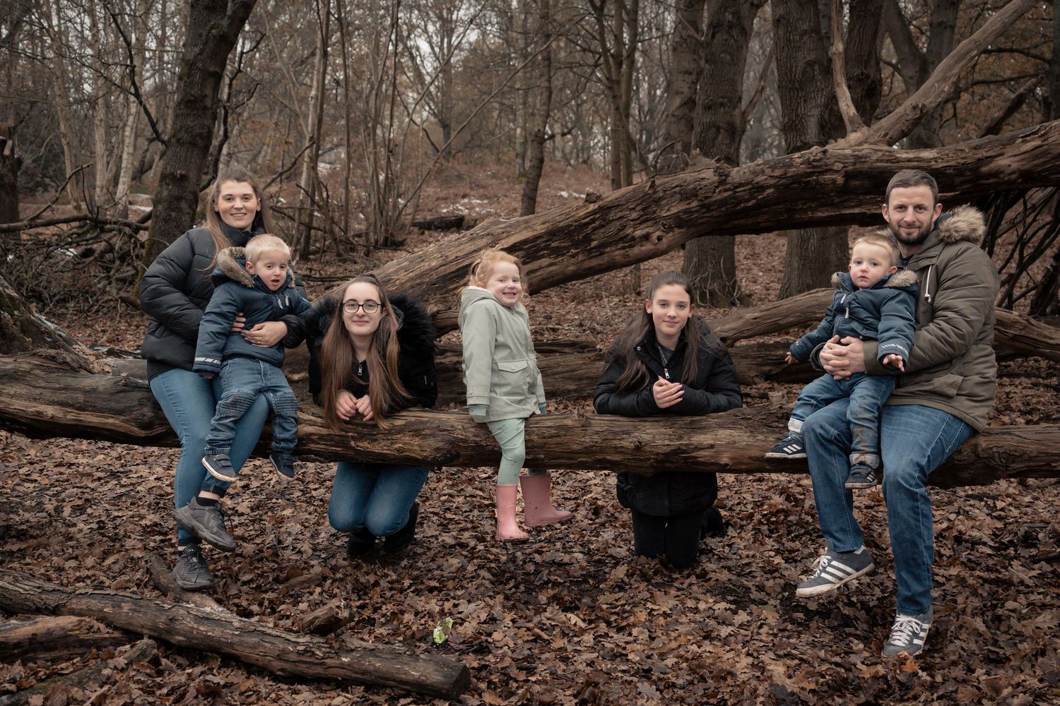 Group sitting together on fallen logs in an autumn forest setting.
