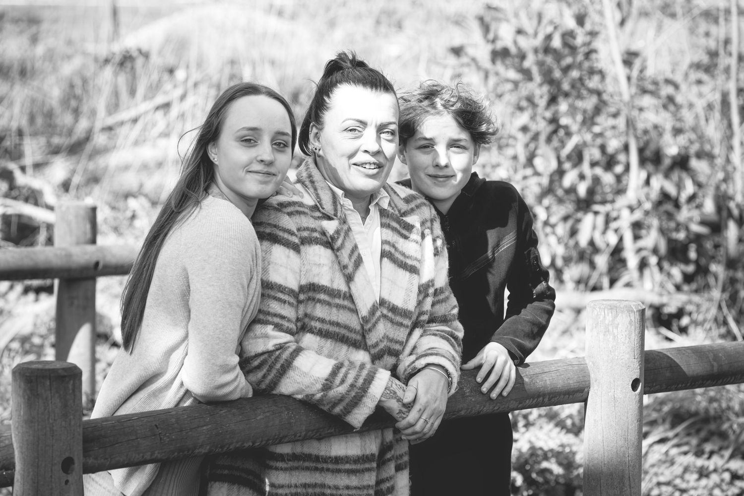 Vintage black and white photograph of three people sitting together on a wooden fence.