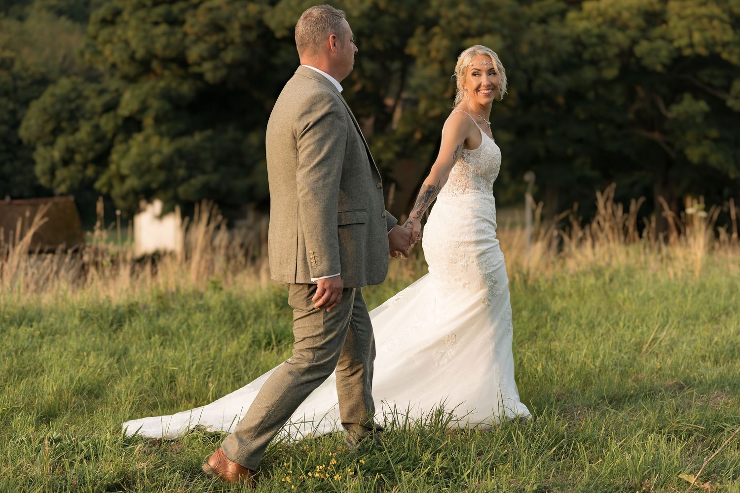 Couple walking through golden field at sunset in wedding attire.