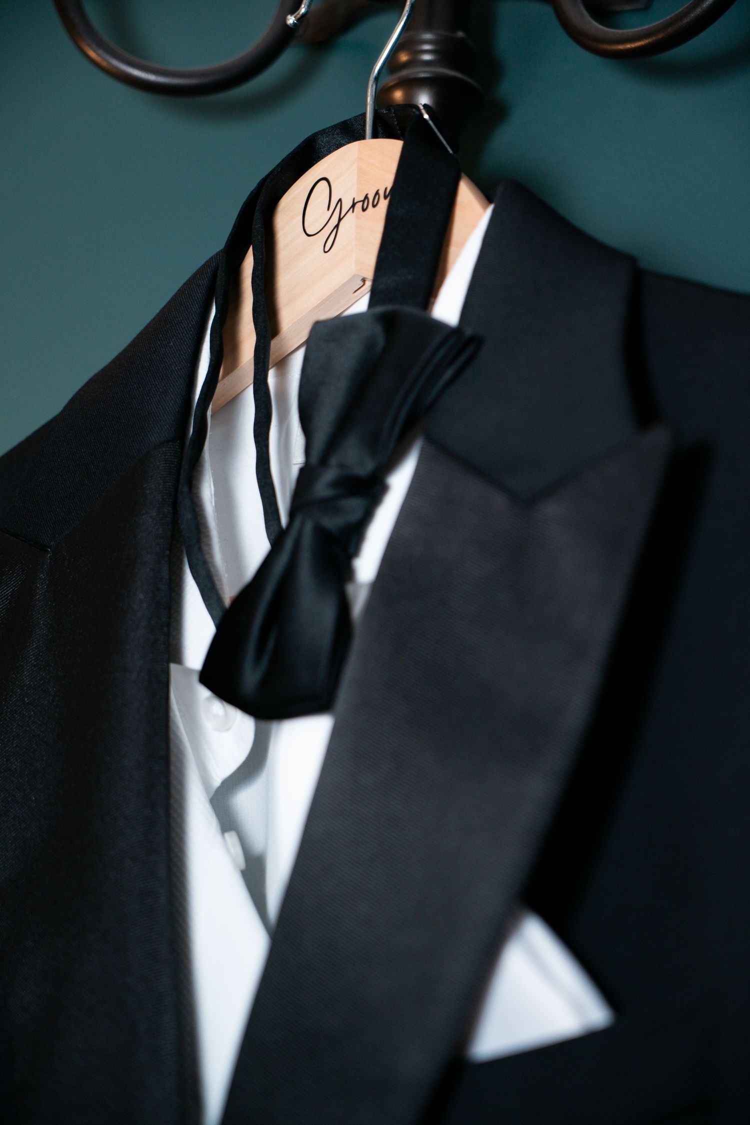 A formal black tuxedo with bow tie and white pocket square hanging on a wooden hanger.