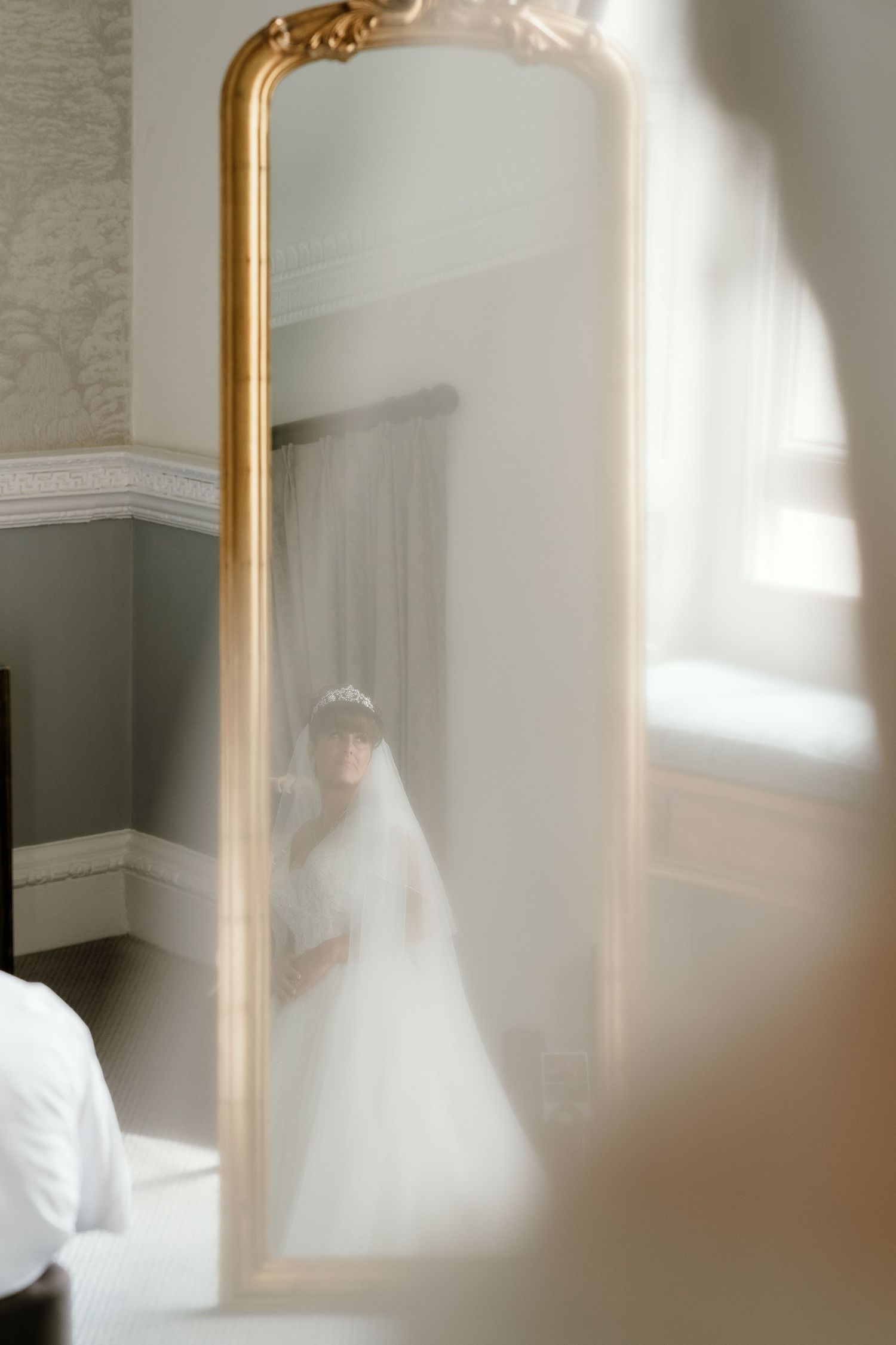 Ethereal wedding dress reflection in a gold-framed mirror with natural window light.