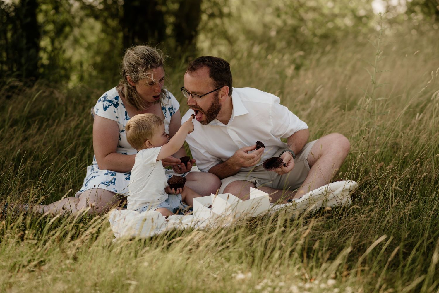 Family having picnic on blanket in summer meadow.