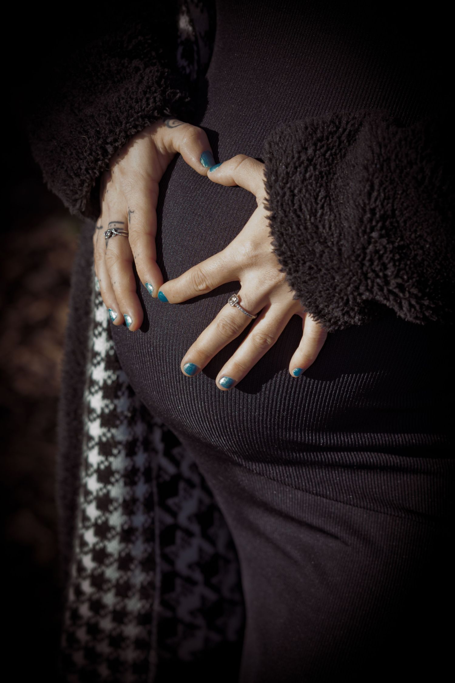 Close-up of hands with rings against dark textured background creating heart shape with fingers.
