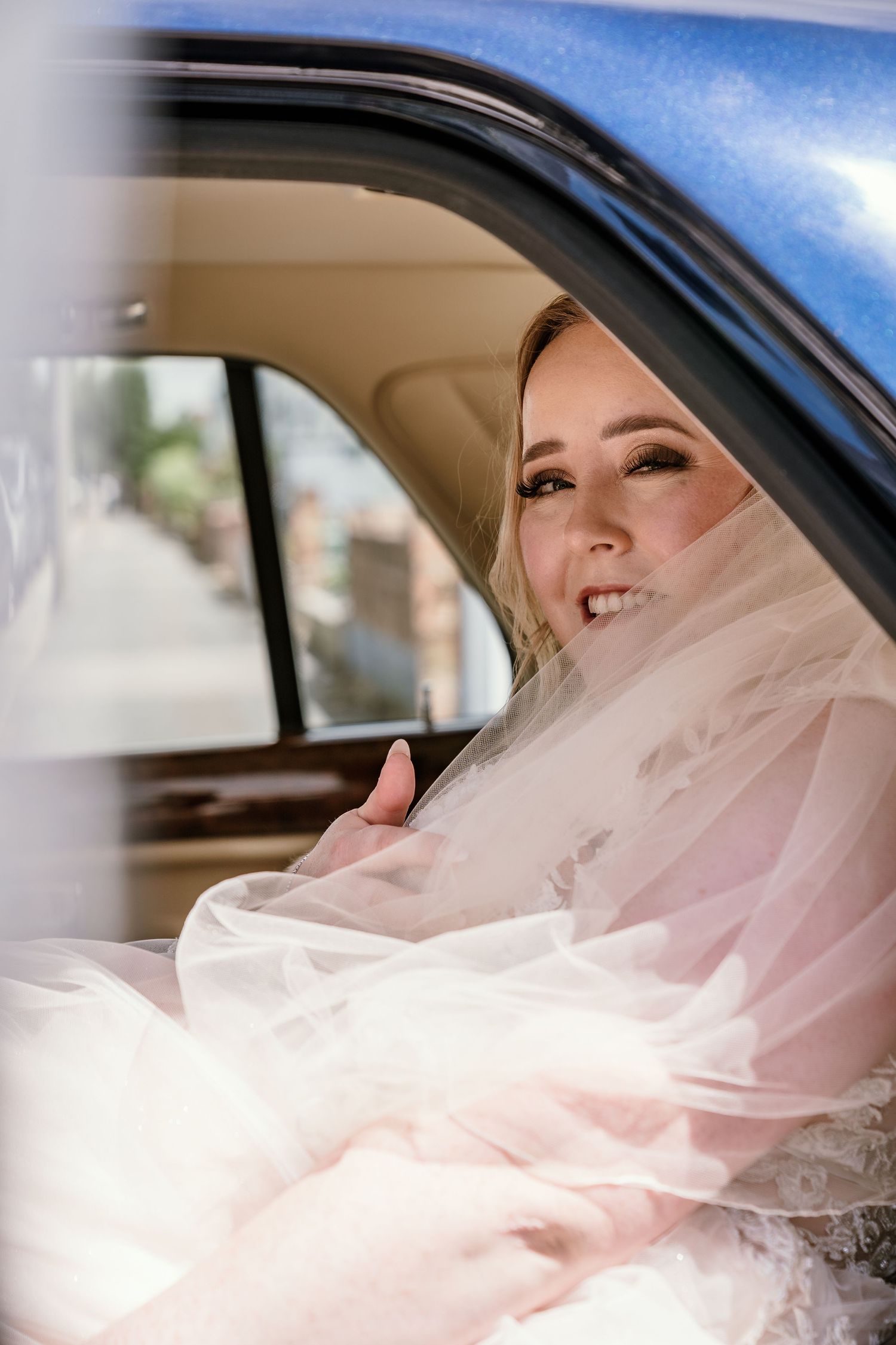 A joyful wedding moment captured through a car window showing a bride wearing a delicate veil.