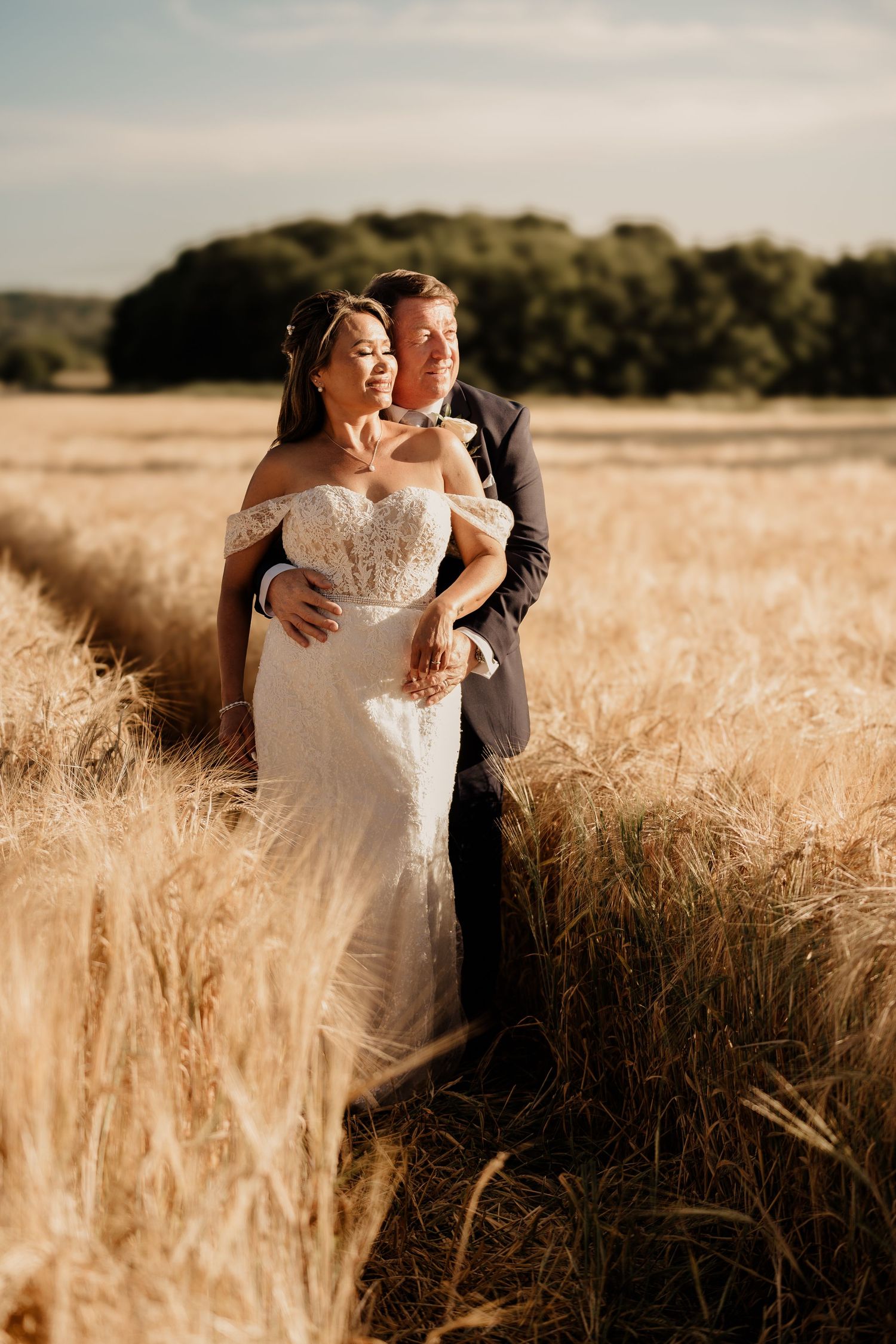 Couple embraces in golden wheat field during sunset photoshoot.