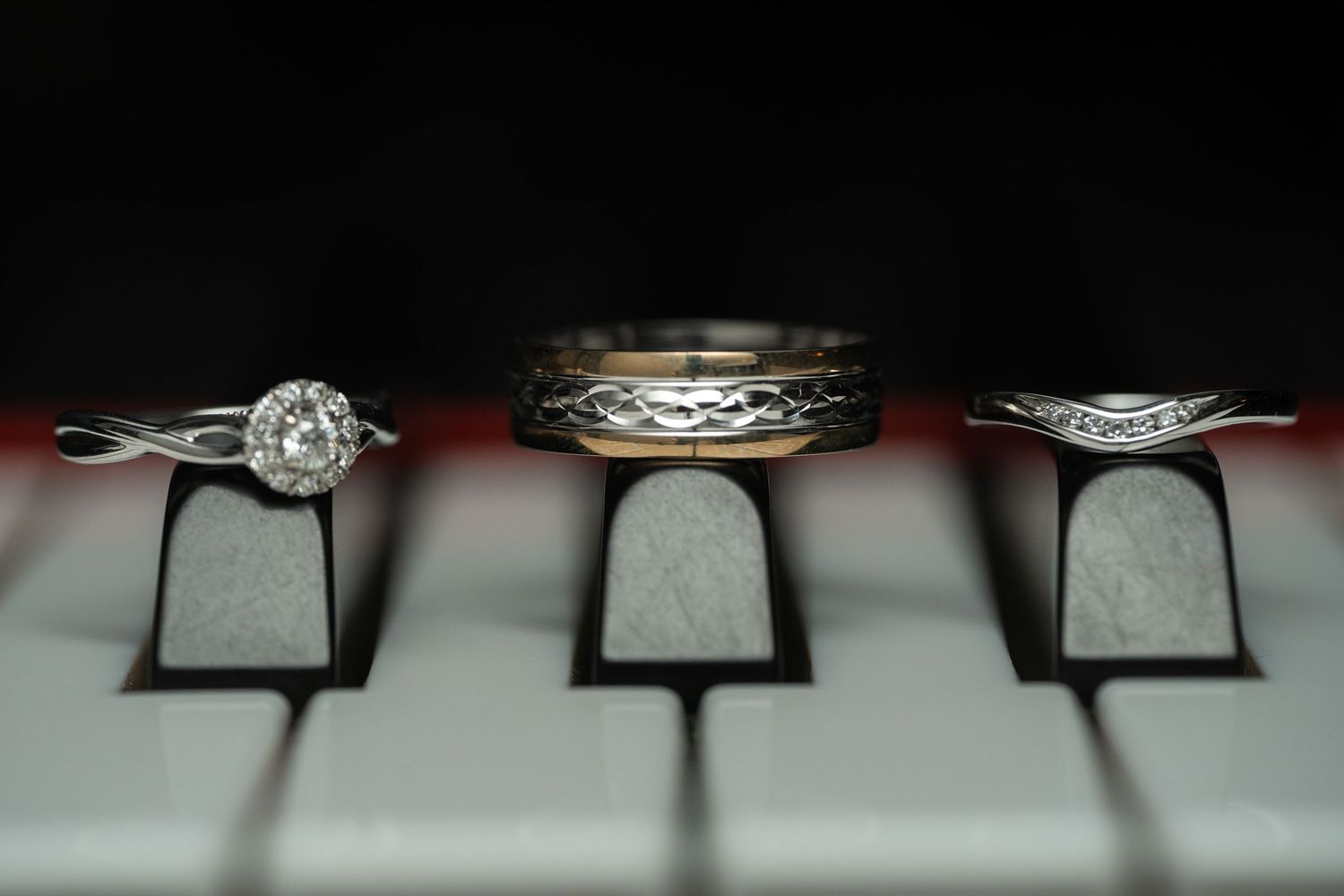 Three wedding rings artistically arranged on piano keys showing intricate metalwork details.