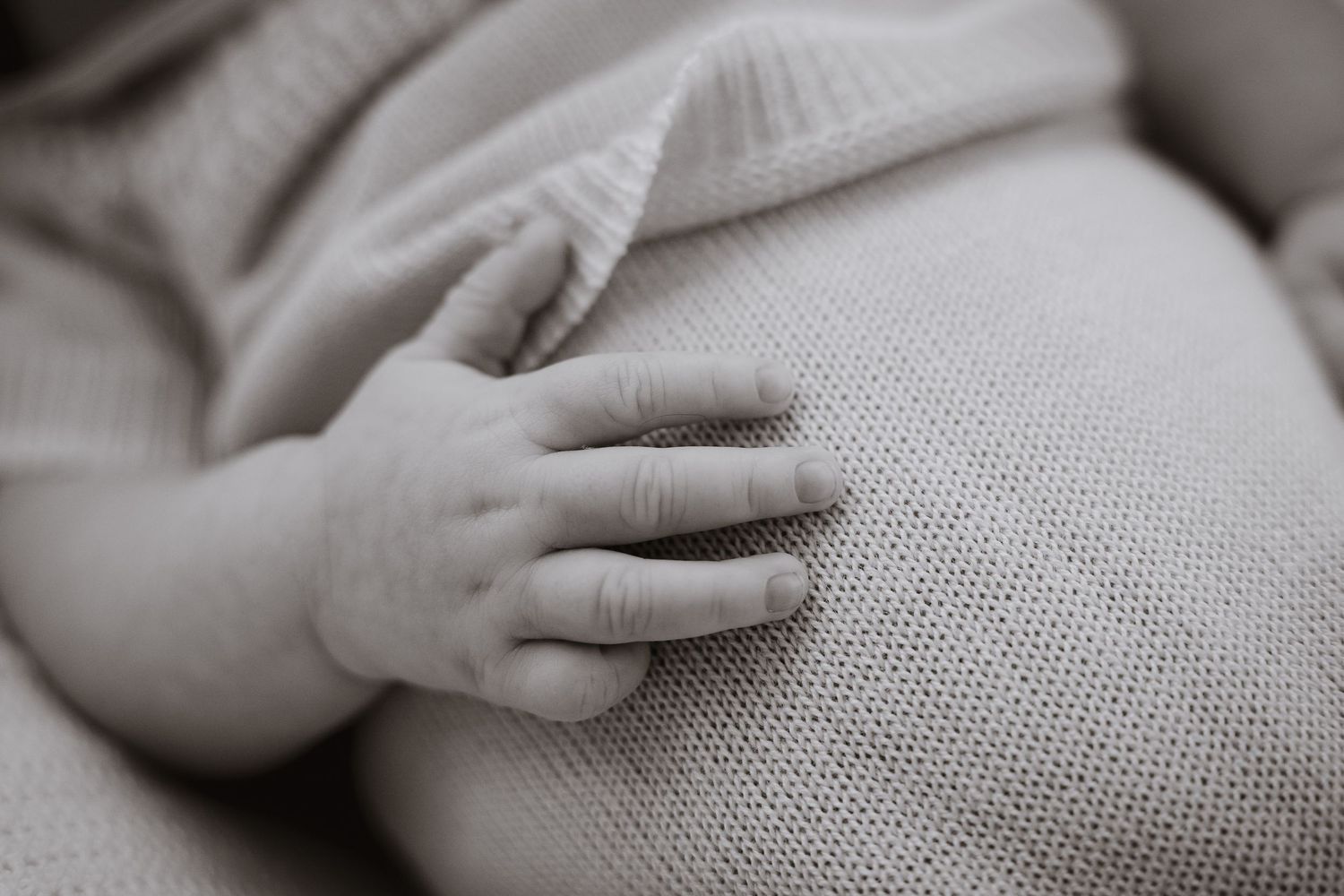 Small infant hand grasps gray fabric in black and white photograph.