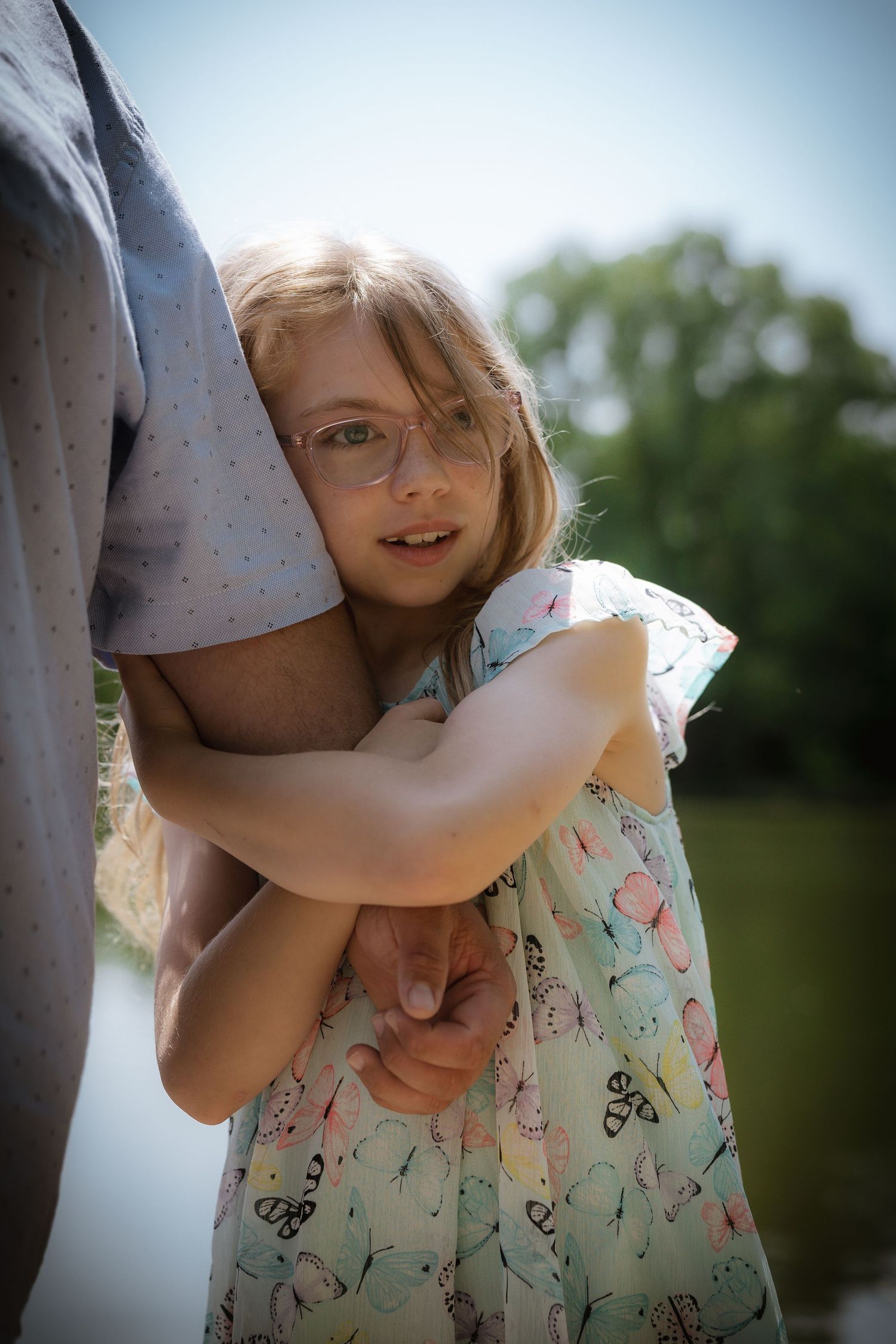 Person in a floral dress hugging another person outdoors on a sunny day.