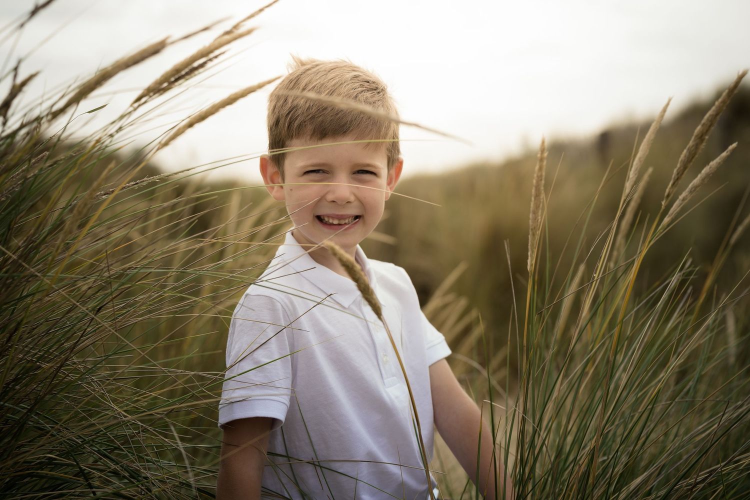 Children playing in tall beach grass during golden hour.