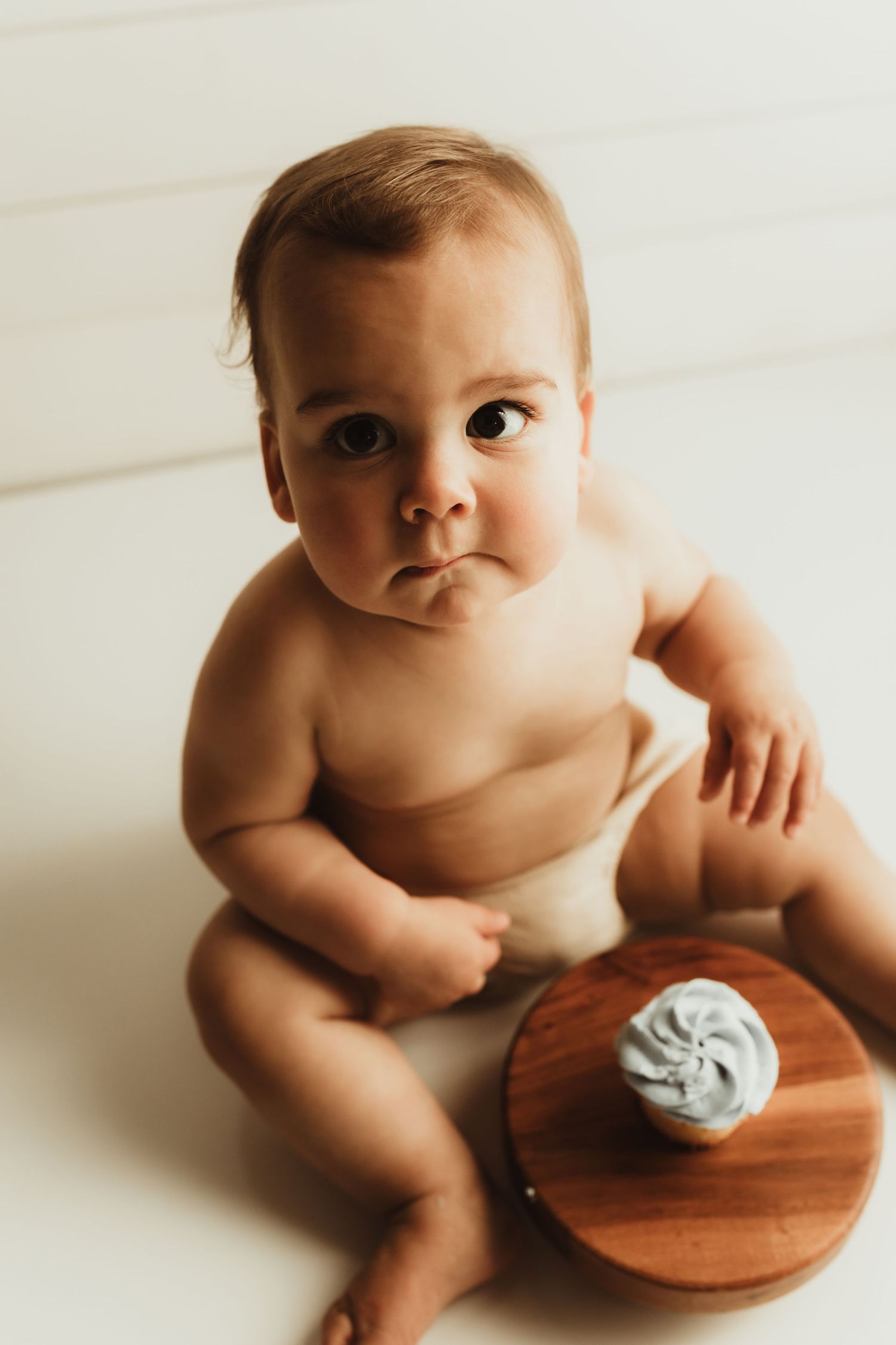 Baby sitting on wooden surface with soft grey toy in artistic portrait series.