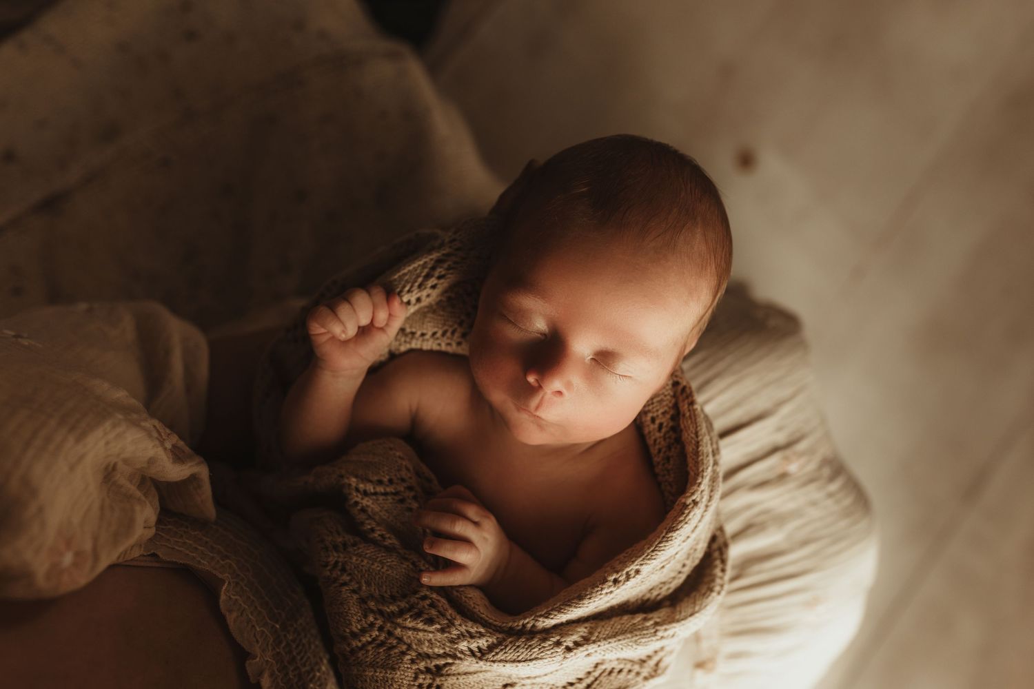Sleeping infant nestled in soft knitted fabric with warm lighting.