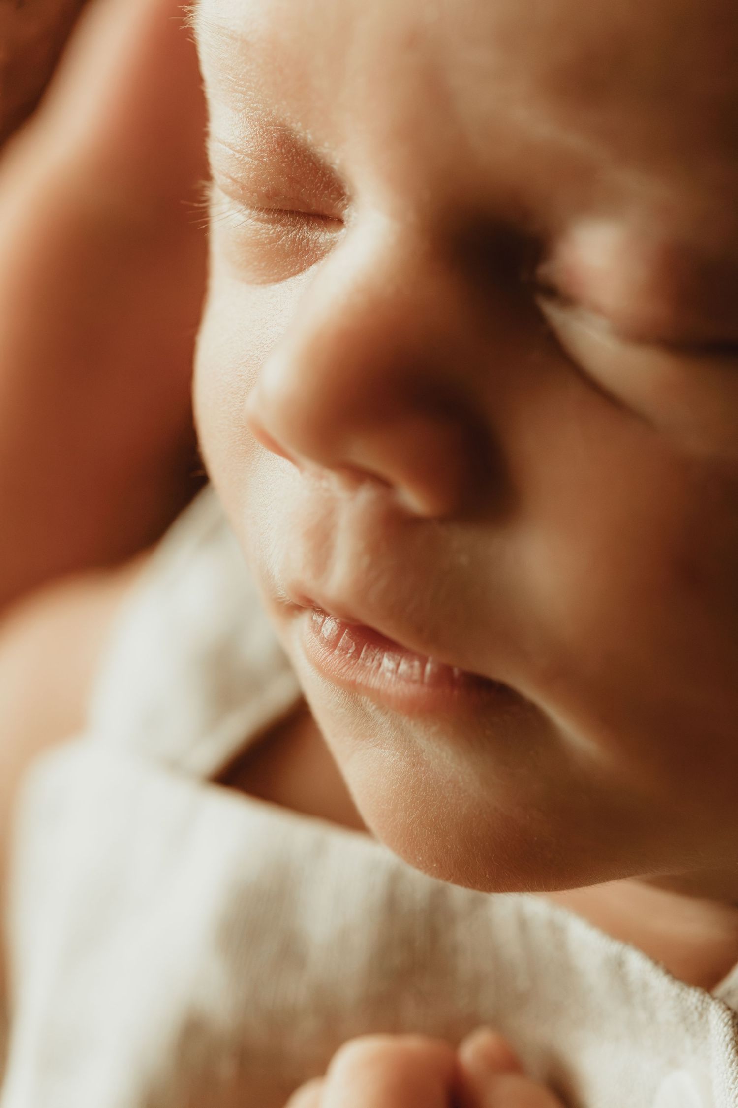 Close-up of a sleeping newborn baby with delicate features, wrapped in a soft white blanket.