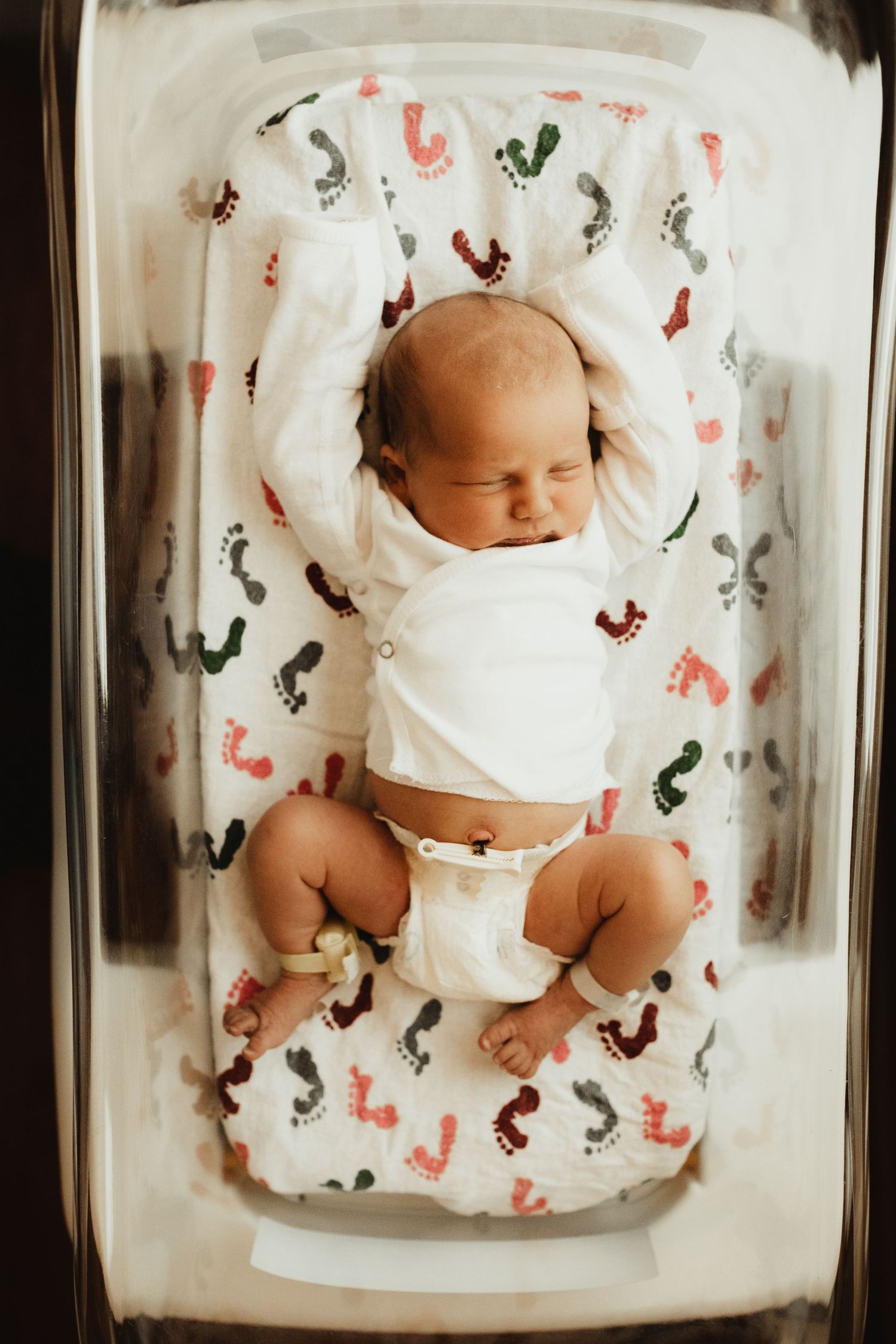 An overhead view of newborn twins sleeping side by side on a white and gray nursery blanket with fox print pattern.