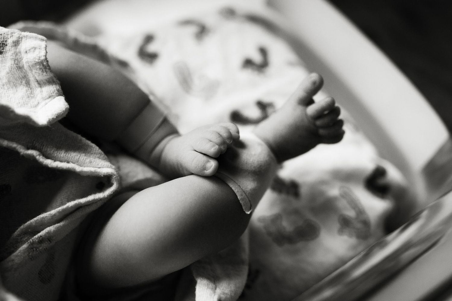 Black and white close-up photo of a newborn baby's tiny feet and hands resting peacefully.