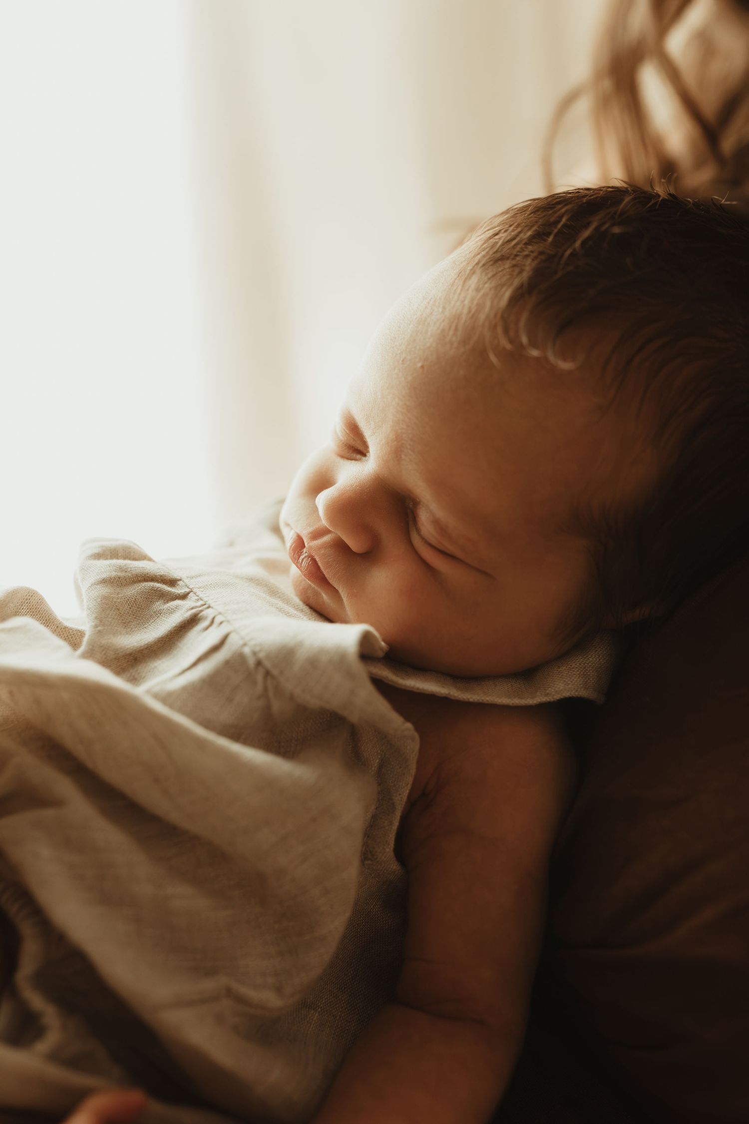 A peaceful newborn baby sleeping soundly, wrapped in a soft linen cloth in warm natural light.