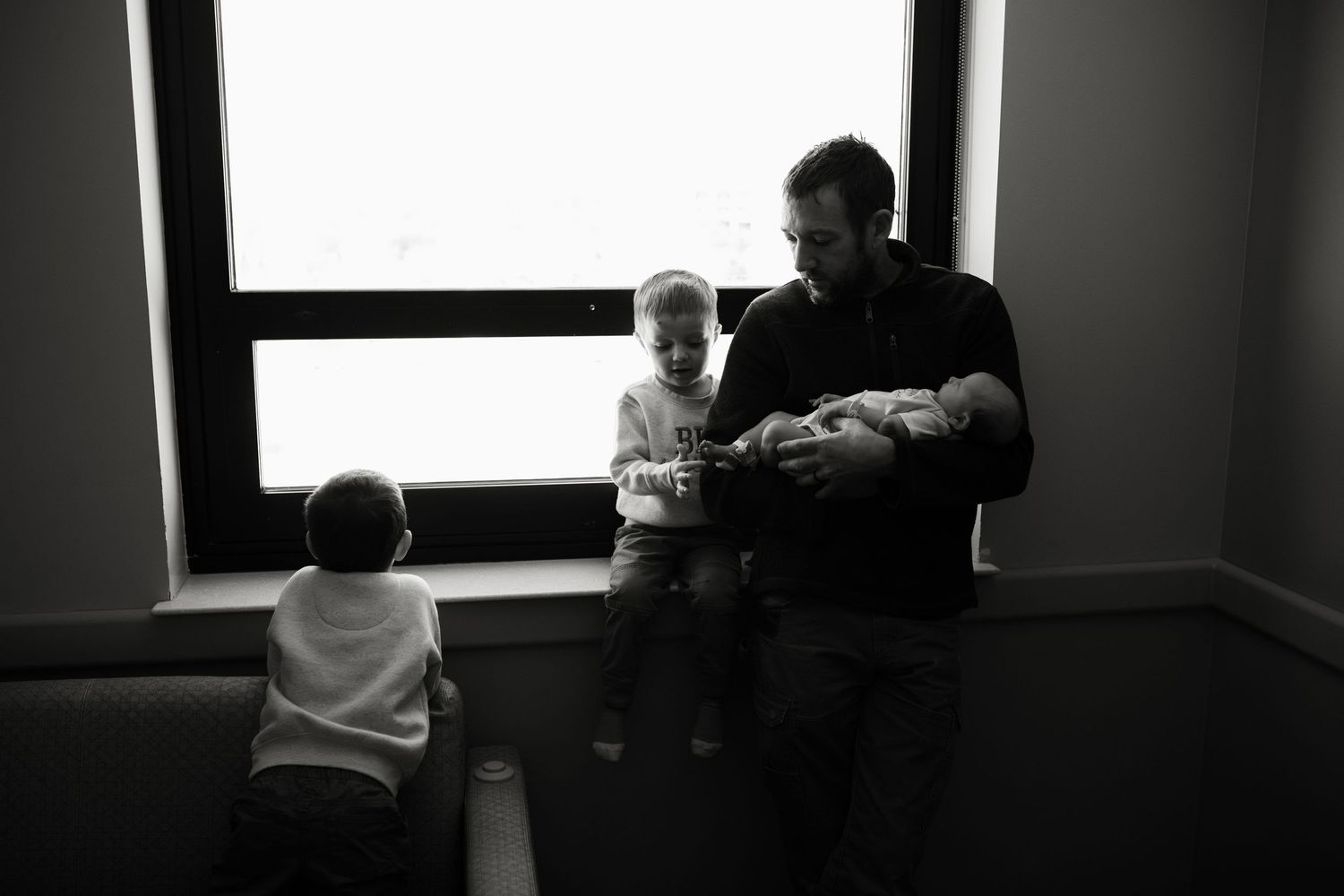 A high contrast black and white photo shows a dark silhouette of a person looking out a bright window.