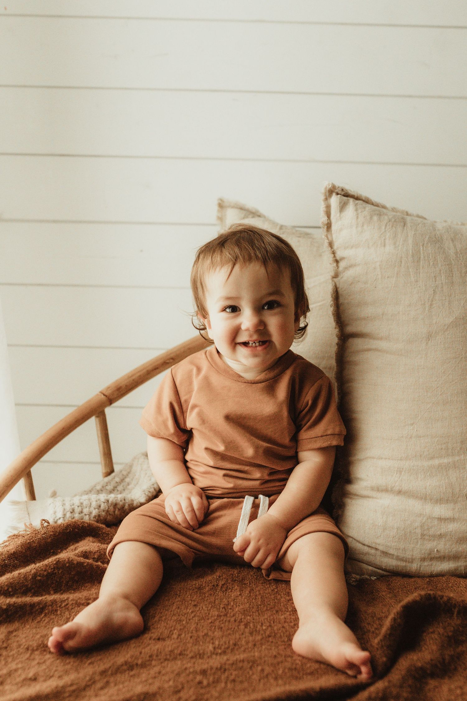 A sequence of candid photos showing a small child in brown clothing sitting on a brown blanket against beige cushions.