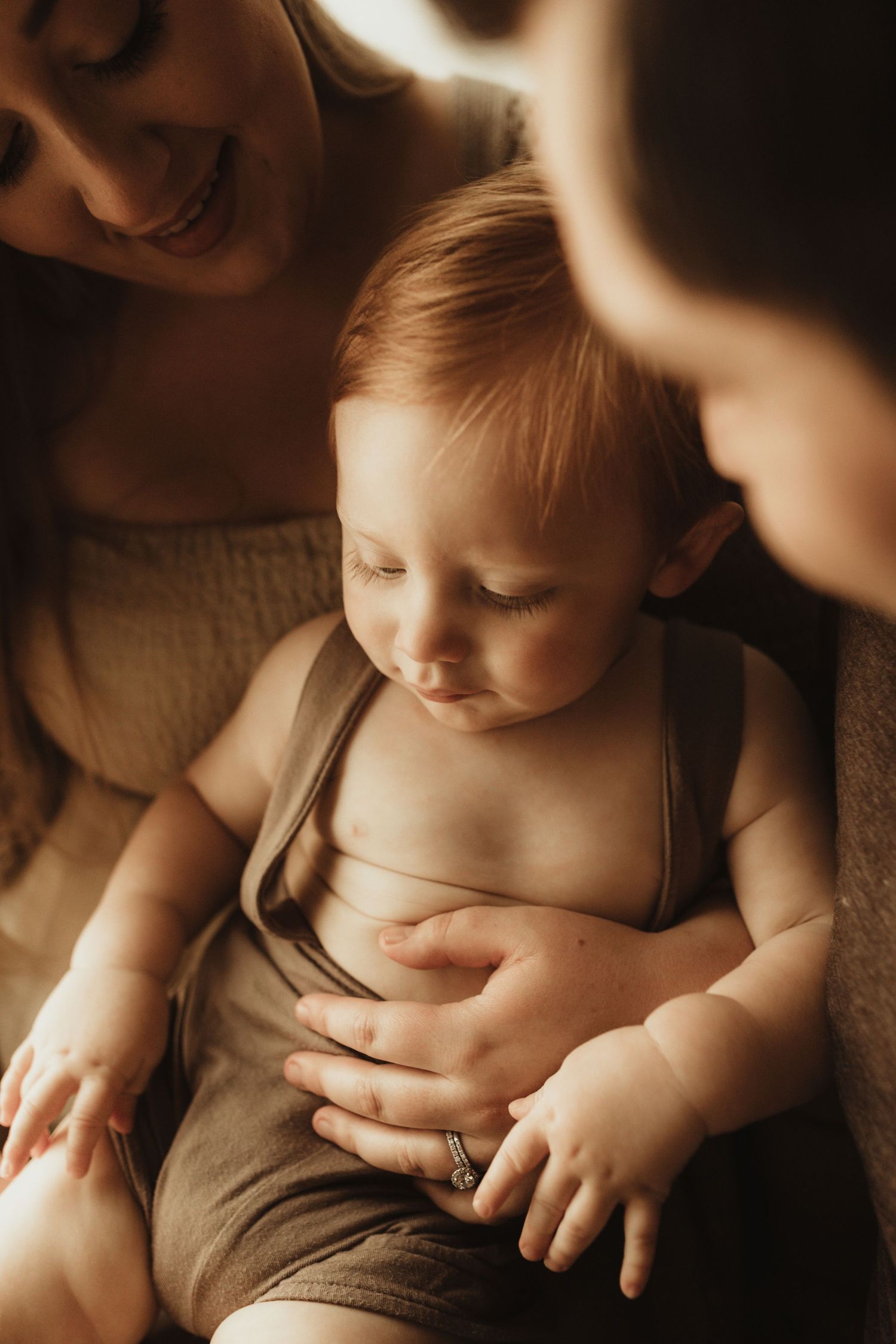 Artistic sepia-toned close-up photos of a baby's bare torso and hands in warm lighting.