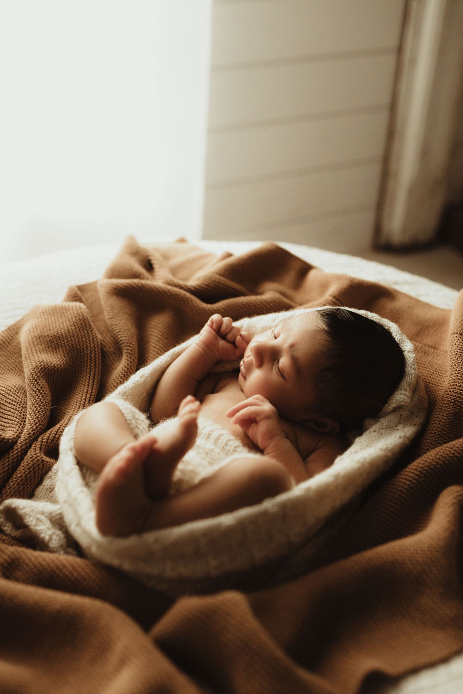 A row of photos showing a peaceful baby swaddled in a soft brown blanket while sleeping in natural window light.