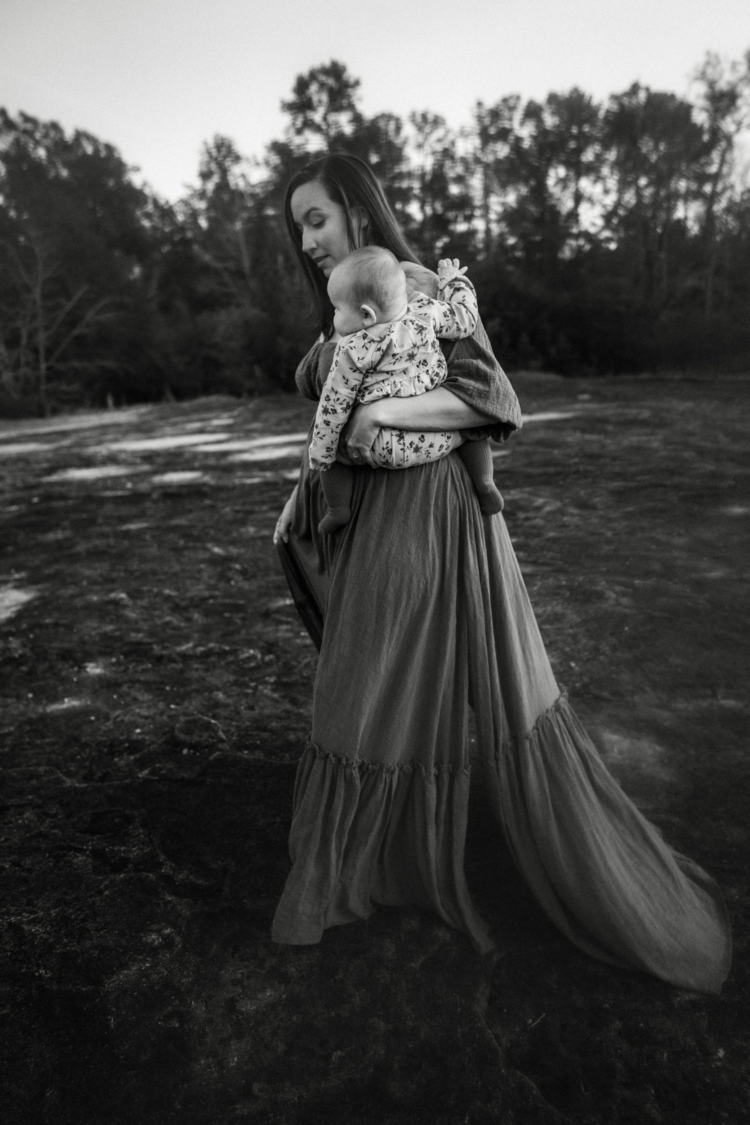 A figure in an elegant floral dress twirls gracefully in a grassy outdoor setting at dusk.