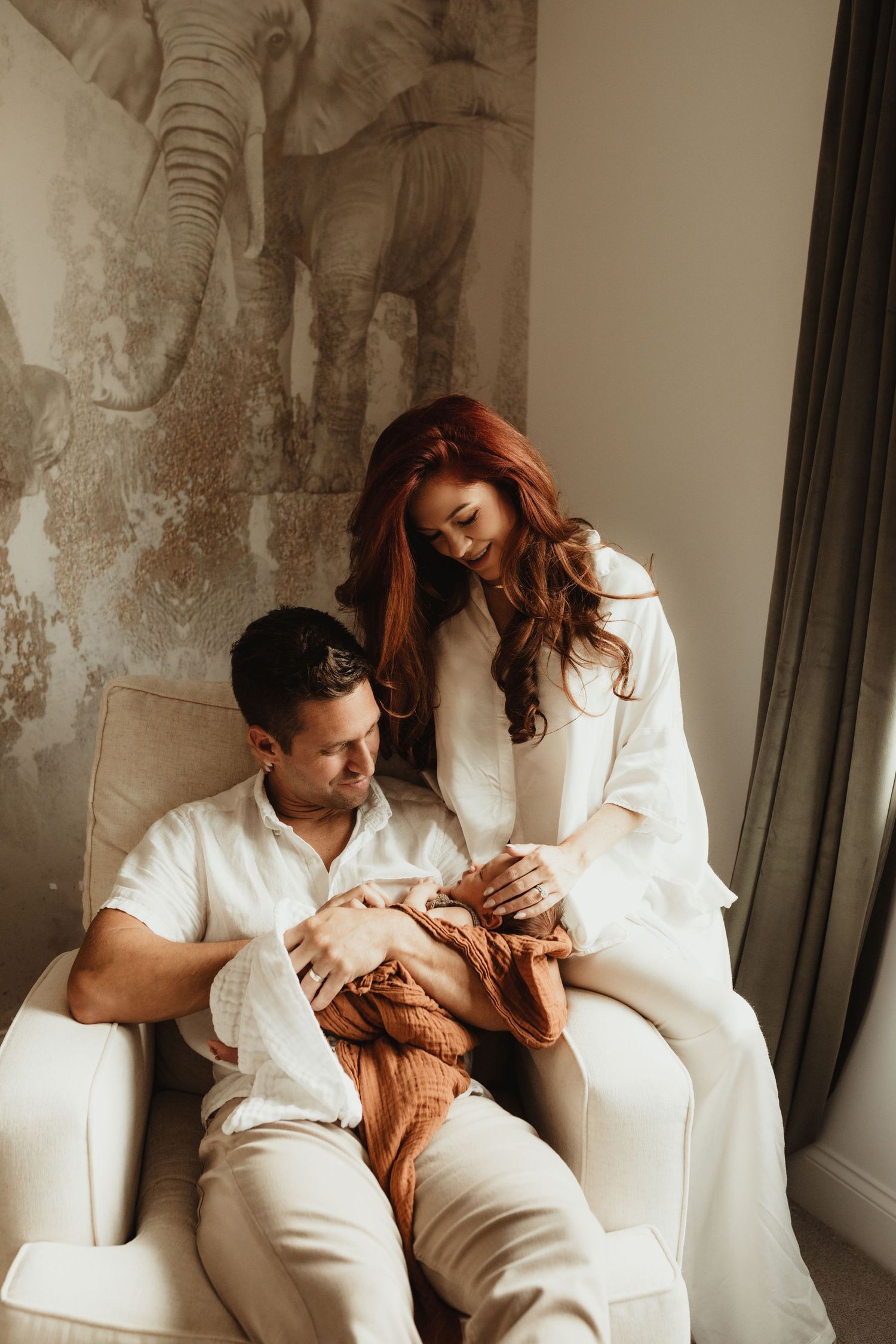Warm-toned family portrait in a room with an elephant wall mural.