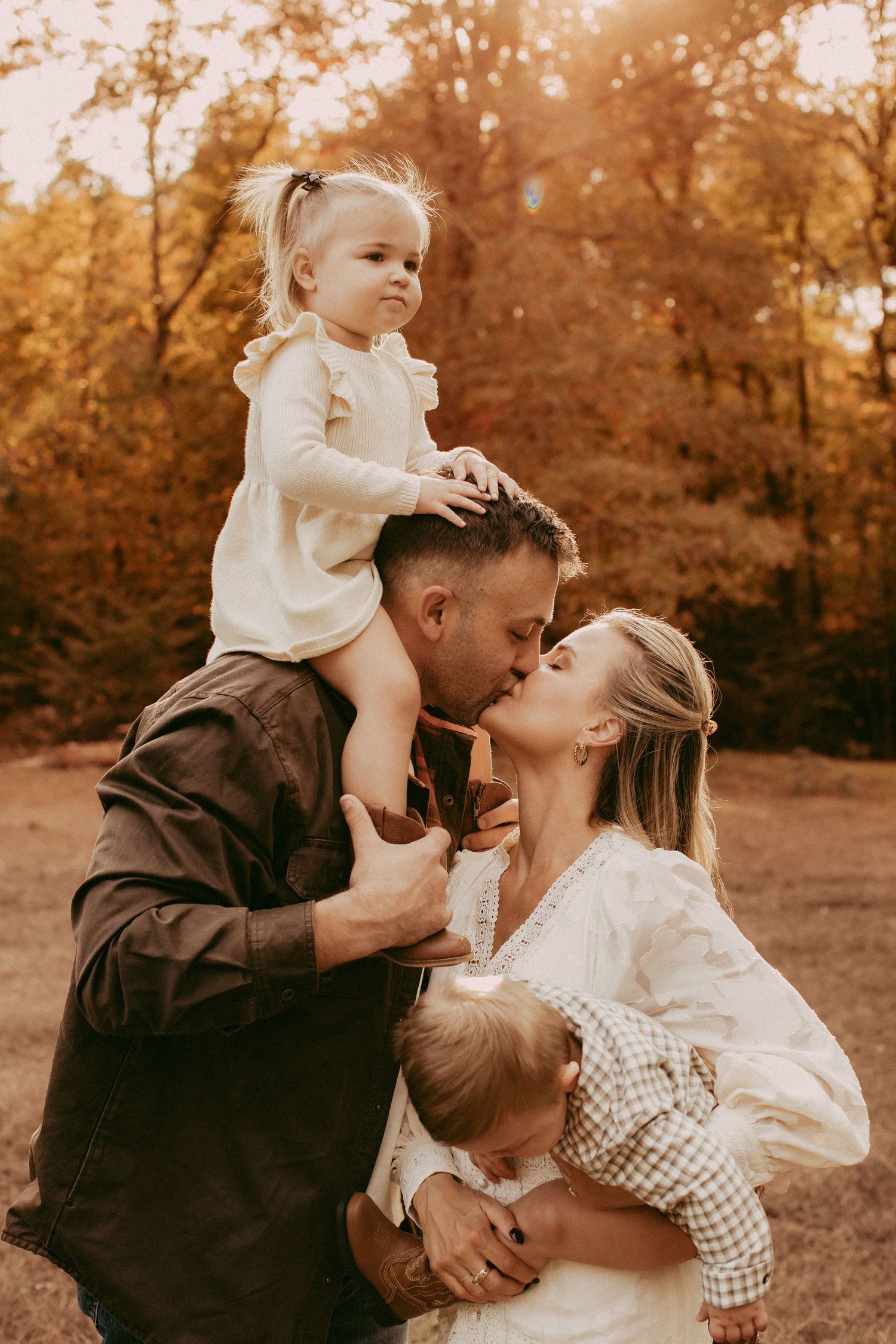 Family of four sharing a tender kiss during a golden autumn outdoor photo session with two young children.