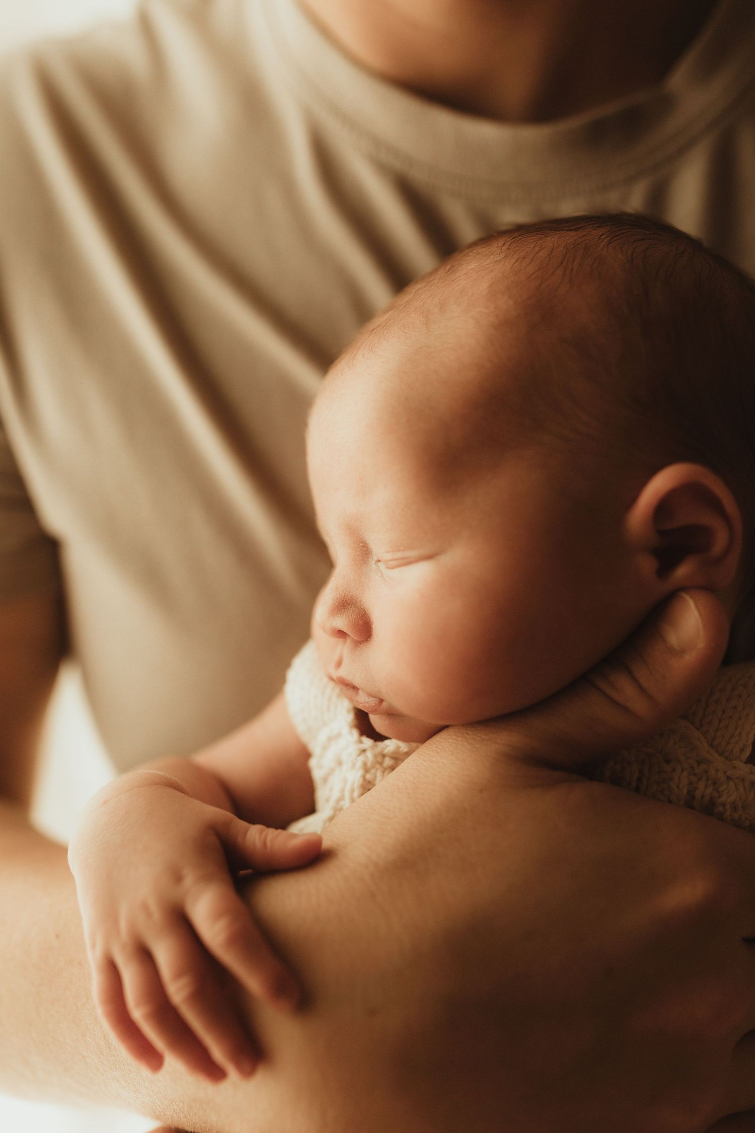 A mother breastfeeding her baby in a warm, intimate setting with soft natural lighting and shallow depth of field.
