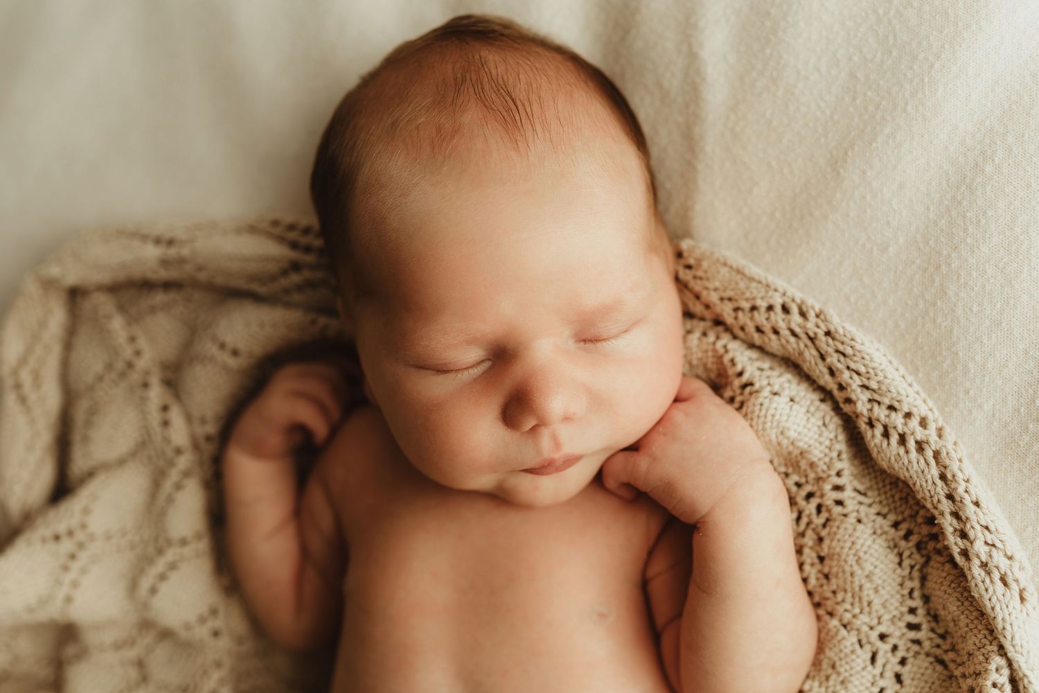 Peaceful newborn baby sleeping wrapped in a soft beige knit blanket during a professional newborn photography session.