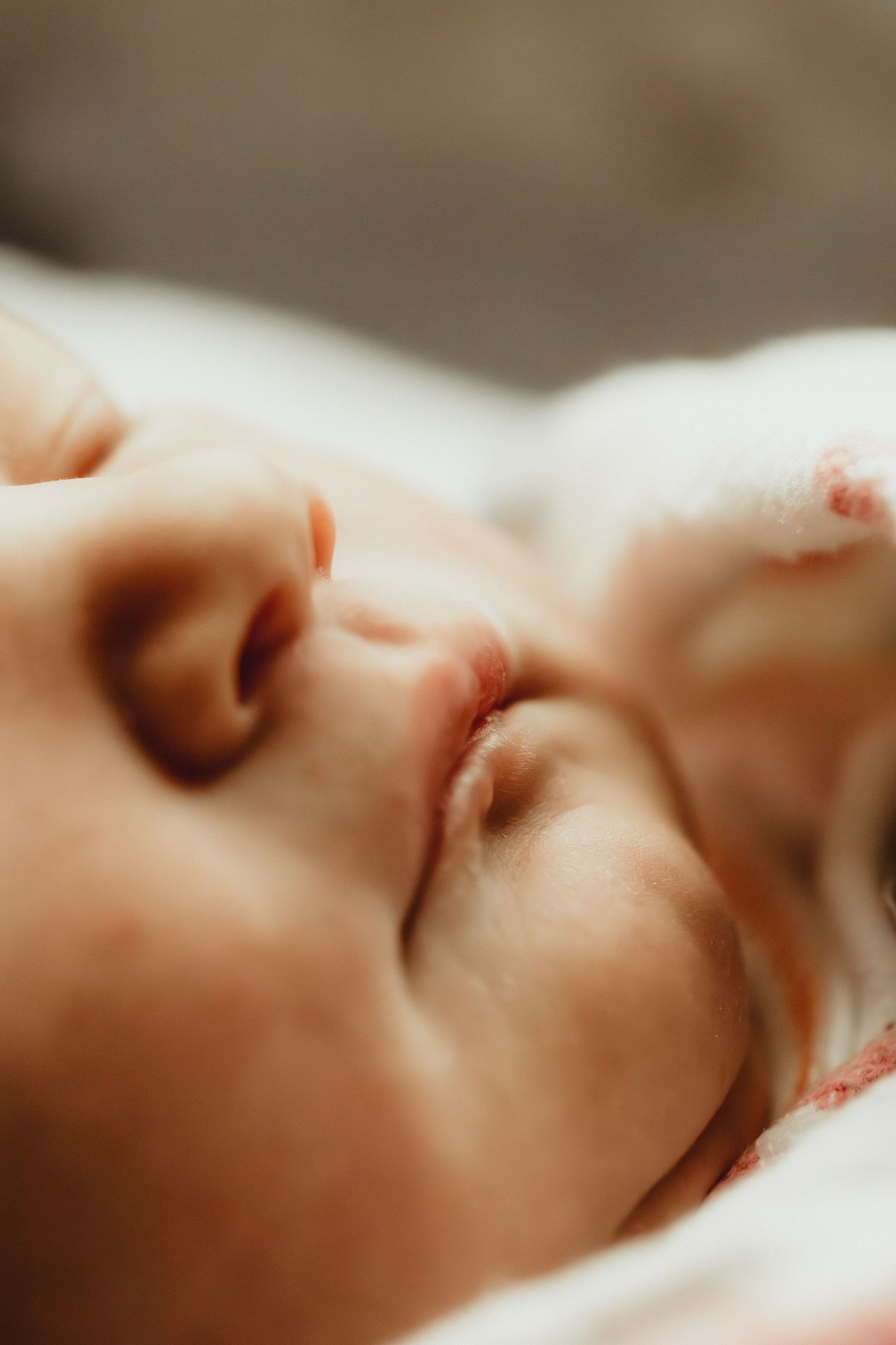 Close-up of a peaceful sleeping newborn baby with soft skin and tiny features resting on a white blanket.