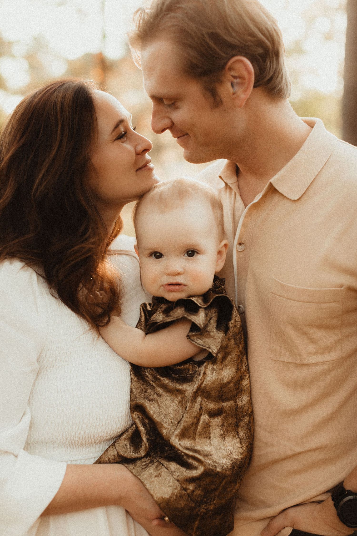 Warm-toned family portrait with young baby captured in soft evening light.