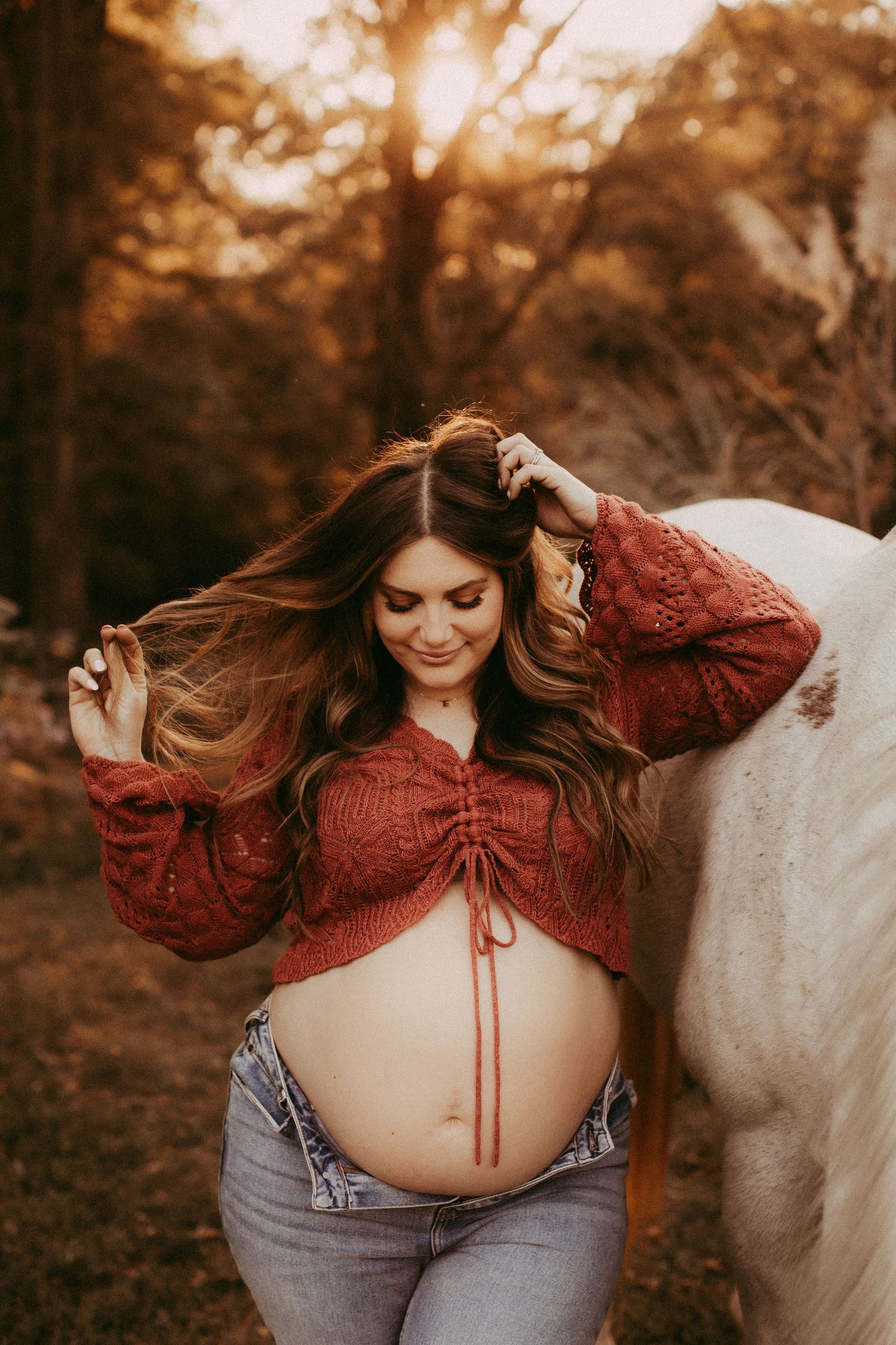 A maternity photoshoot in warm autumn tones featuring a burgundy cropped top and flowing hair at sunset.