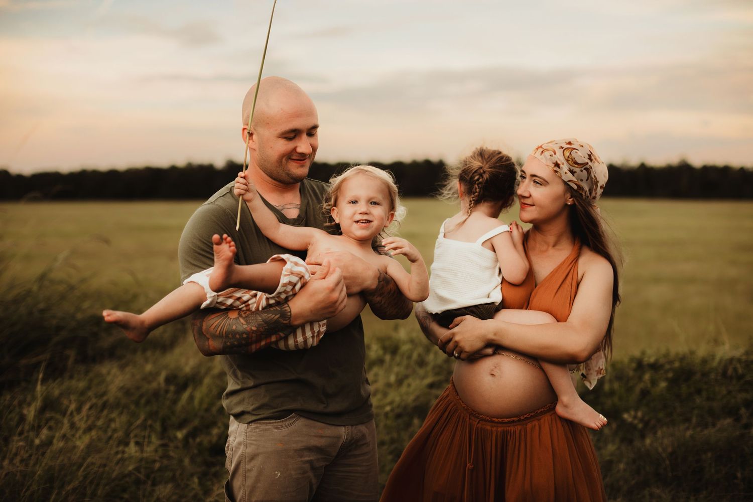 A heartwarming family maternity photoshoot in a golden field at sunset creates intimate moments together.