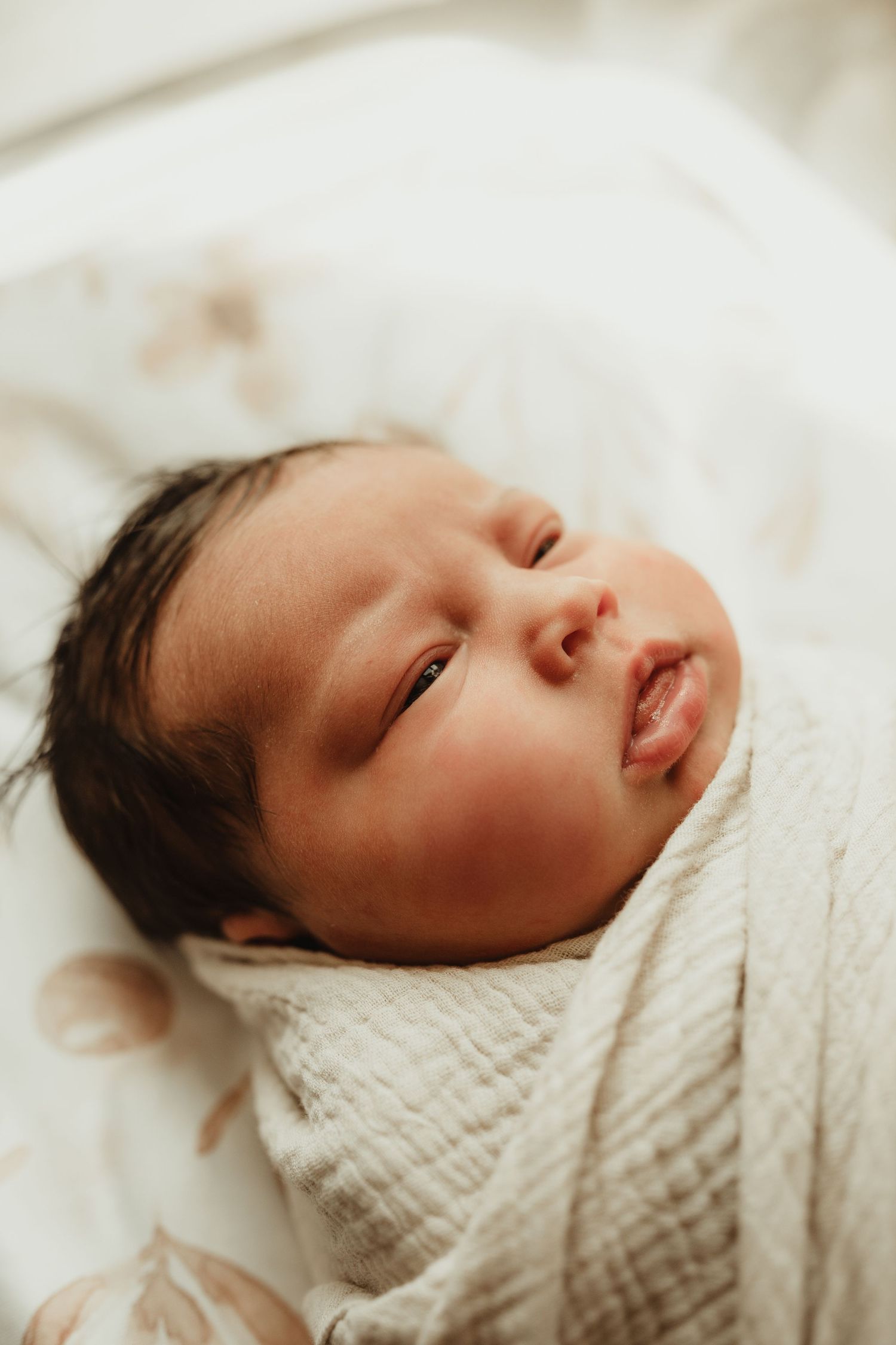 Sleeping newborn baby wrapped in soft white textured blanket in bright natural lighting.