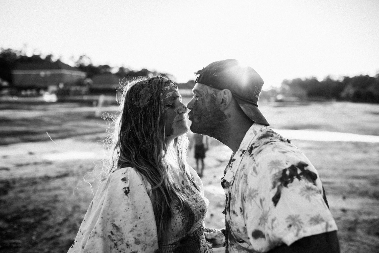 Black and white image of a couple in wedding attire sharing a romantic moment in a sunny outdoor setting.