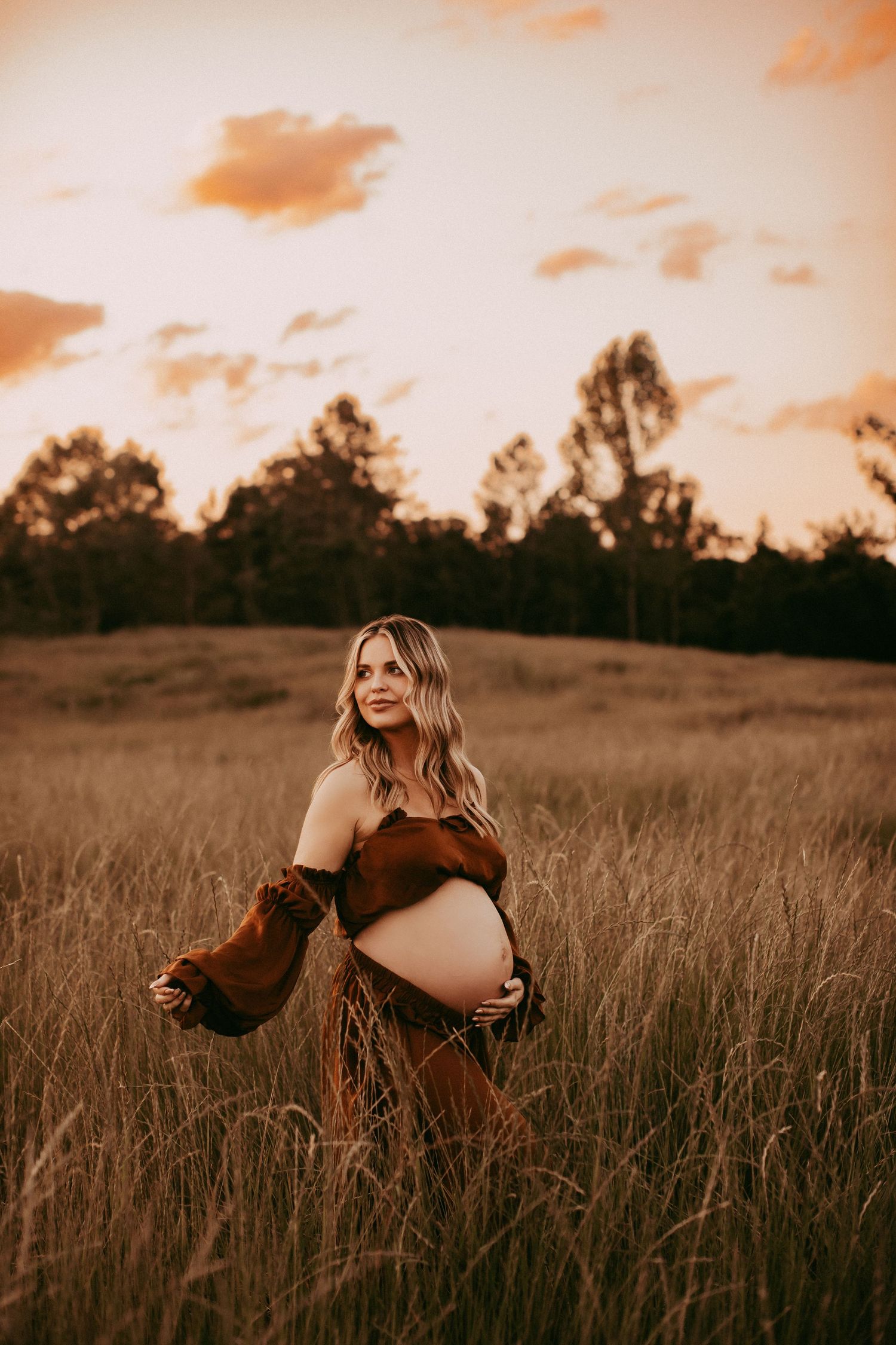 A atmospheric sunset countryside portrait in tall grass field with warm golden lighting and rich orange sky.
