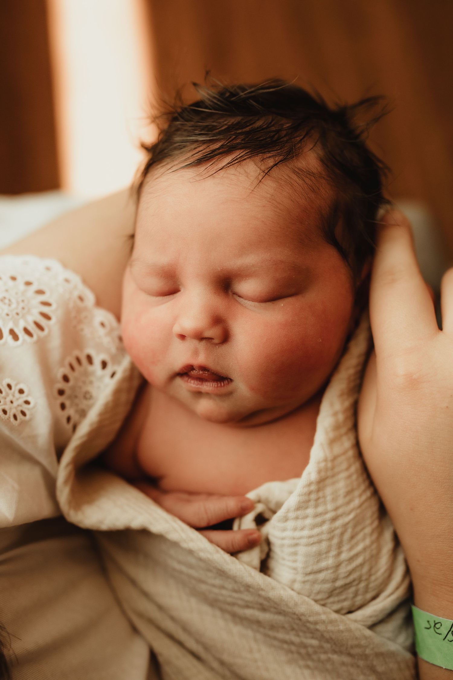 A peaceful sleeping newborn baby wrapped in a soft cream-colored swaddle blanket in warm lighting.