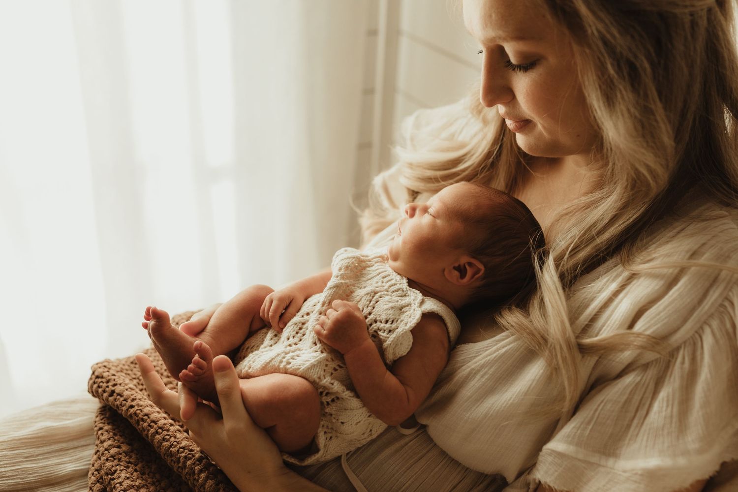 A tender moment between parent and newborn in soft natural window light.