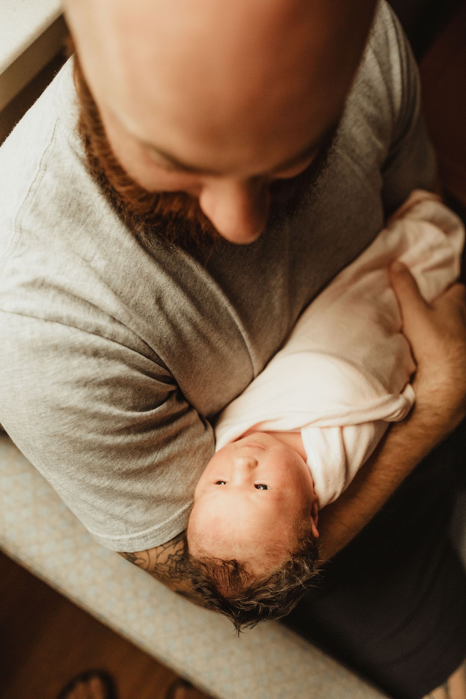 Parent and newborn sharing intimate bonding moment while resting together on dark surface viewed from above.
