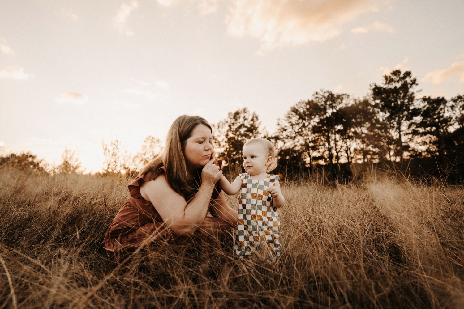 A couple embraces tenderly in a golden sunlit field of tall grass during sunset.