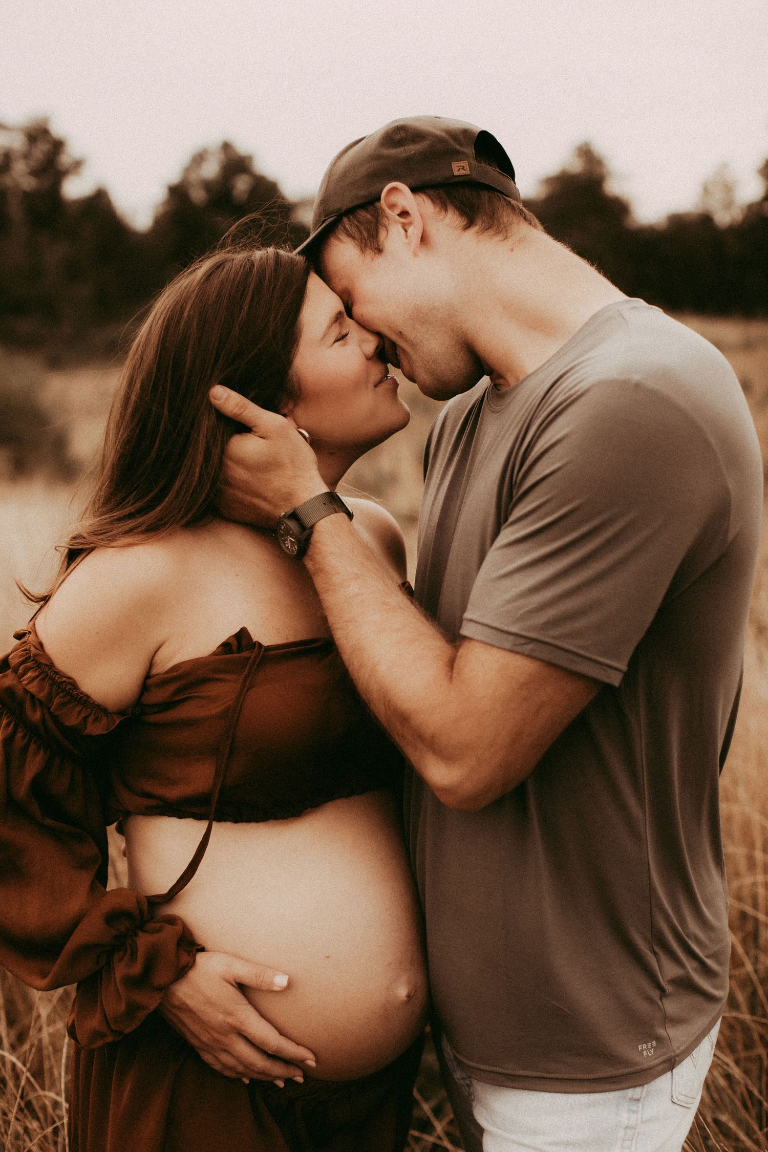 A romantic couple embraces in a golden field during sunset while sharing intimate moments in matching outfits.