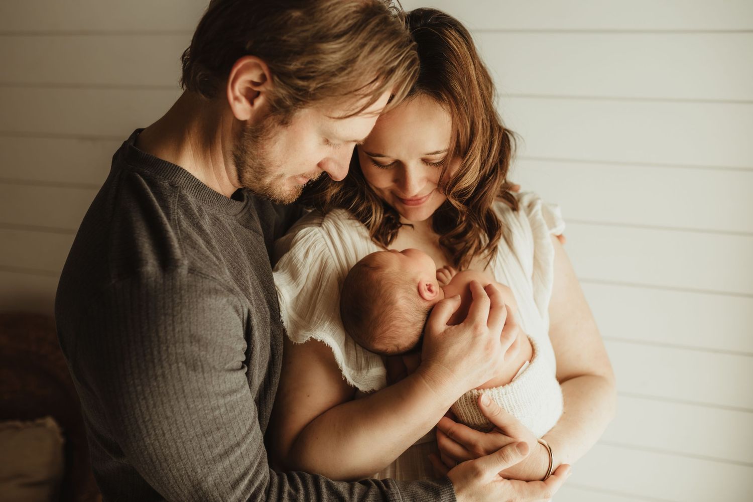 New parents tenderly cradling their newborn baby together, sharing a loving family moment in soft natural light.
