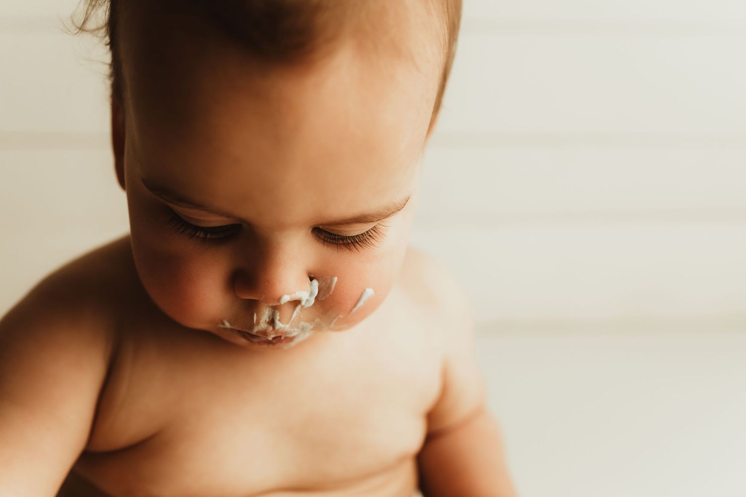 Close-up portrait of a baby with chocolate frosting smeared on their nose against a white background.
