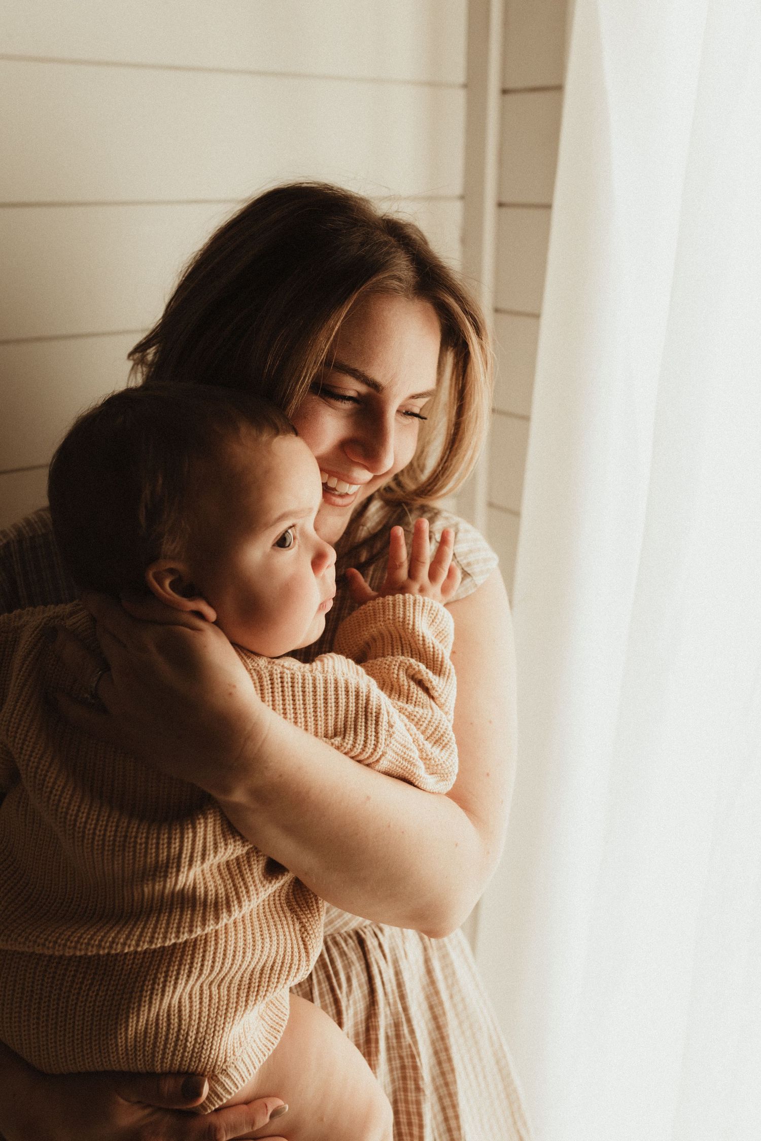 Intimate portrait series showing tender moments between parent and baby in soft beige tones by window light.