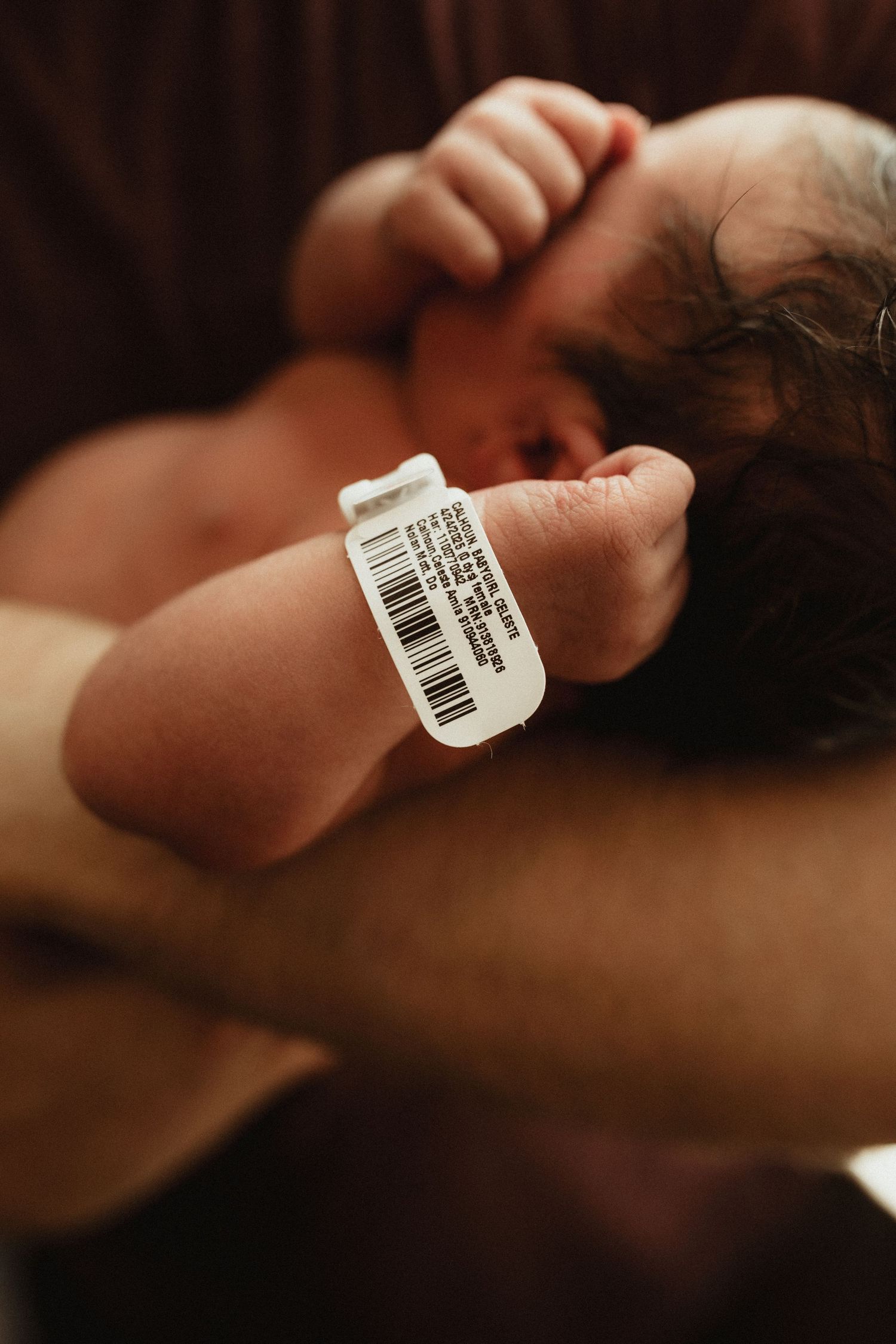 Close-up view of a newborn baby's hand wearing a hospital identification bracelet in warm lighting.